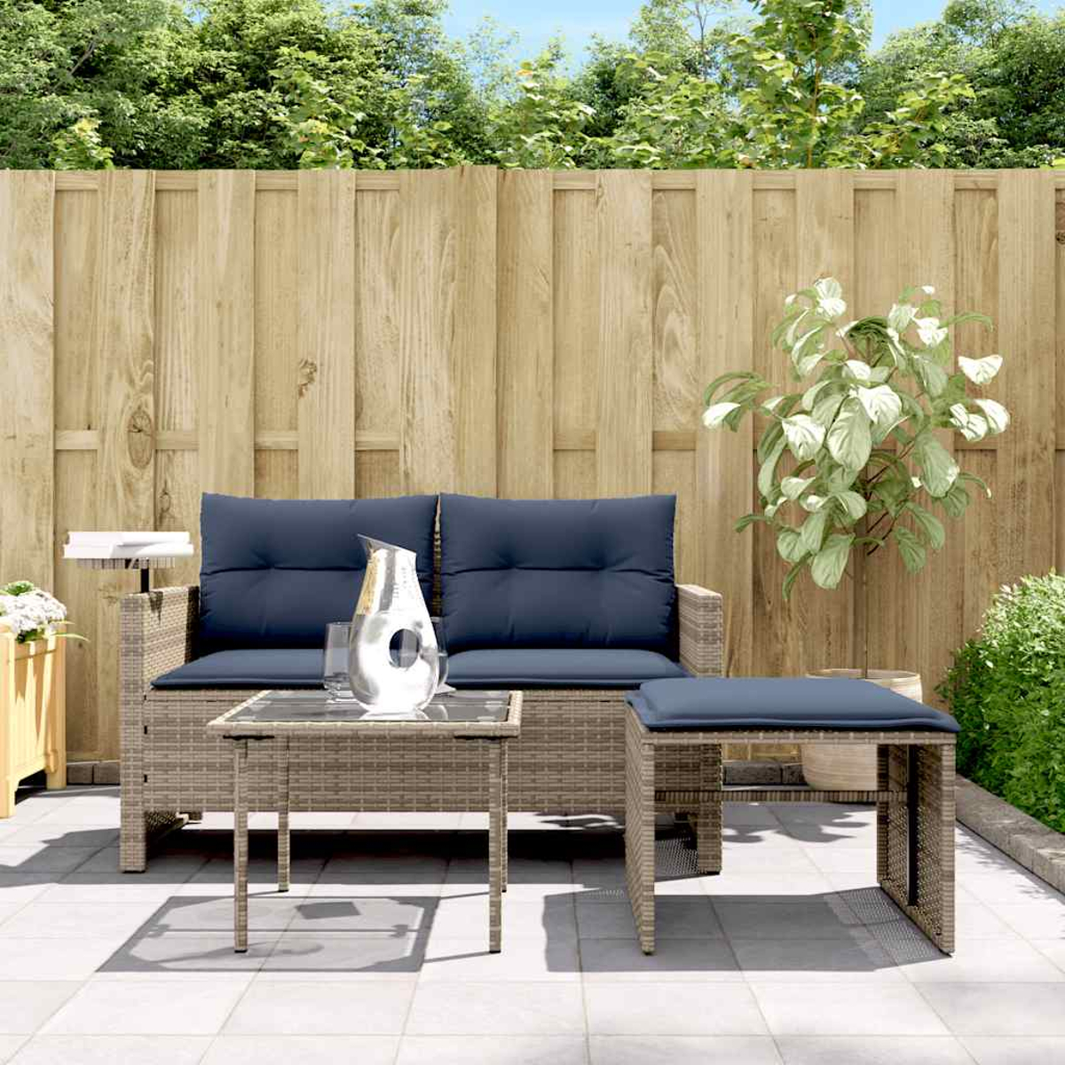 Szene im Freien mit Terrassenmöbeln: eine Couch, ein kleiner Tisch und ein Hocker, alle mit blauen Kissen. Ein Holzzaun im Hintergrund.