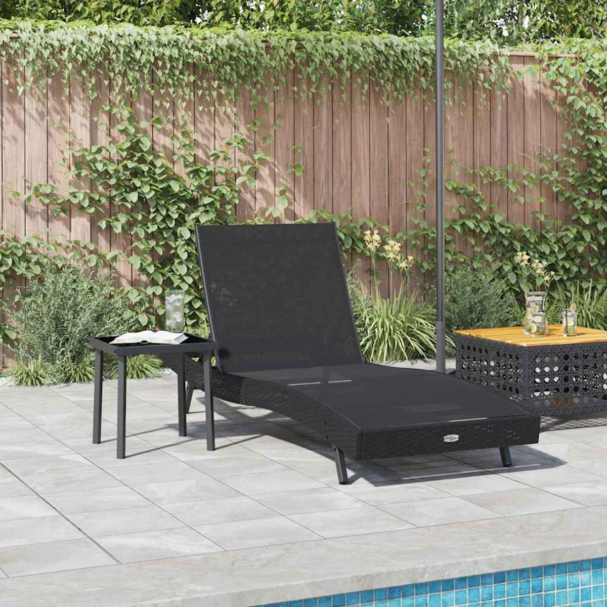 Eine schwarze Sonnenliege und ein kleiner Tisch auf einer Terrasse. Im Hintergrund ein Holzzaun. Am Boden ein Pool.