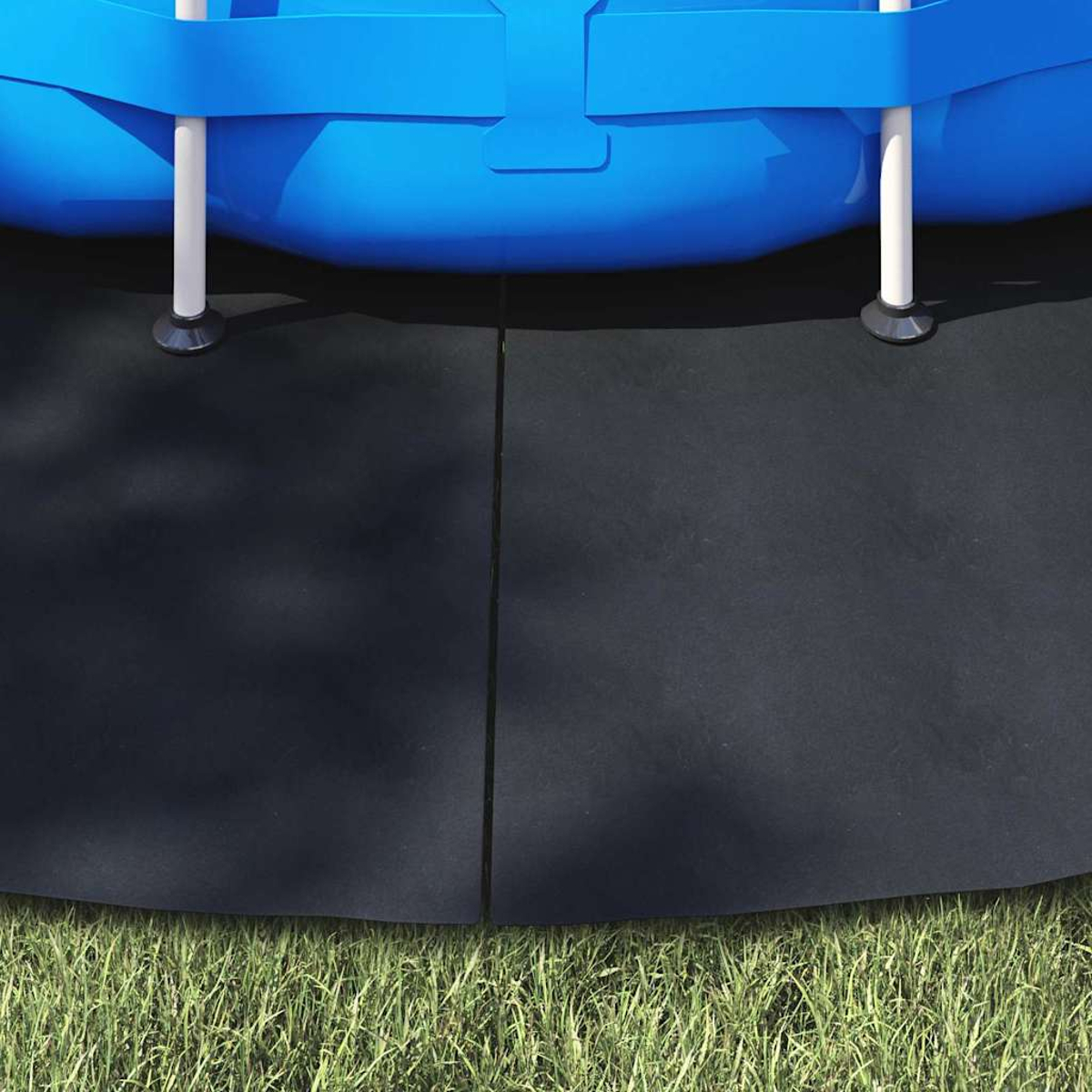Der Rand eines blauen Pools liegt auf schwarzen Matten. Die Matten liegen über grünem Gras. Weiße Beine stützen den Pool.