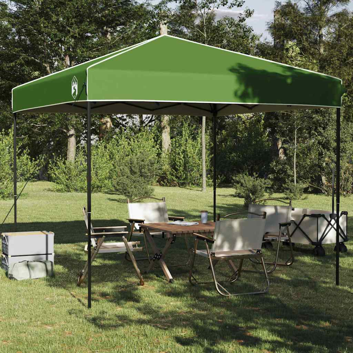 Tenda verde sopra un'area picnic: tavolo, sedie e un carrello, su erba verde, con alberi sullo sfondo.