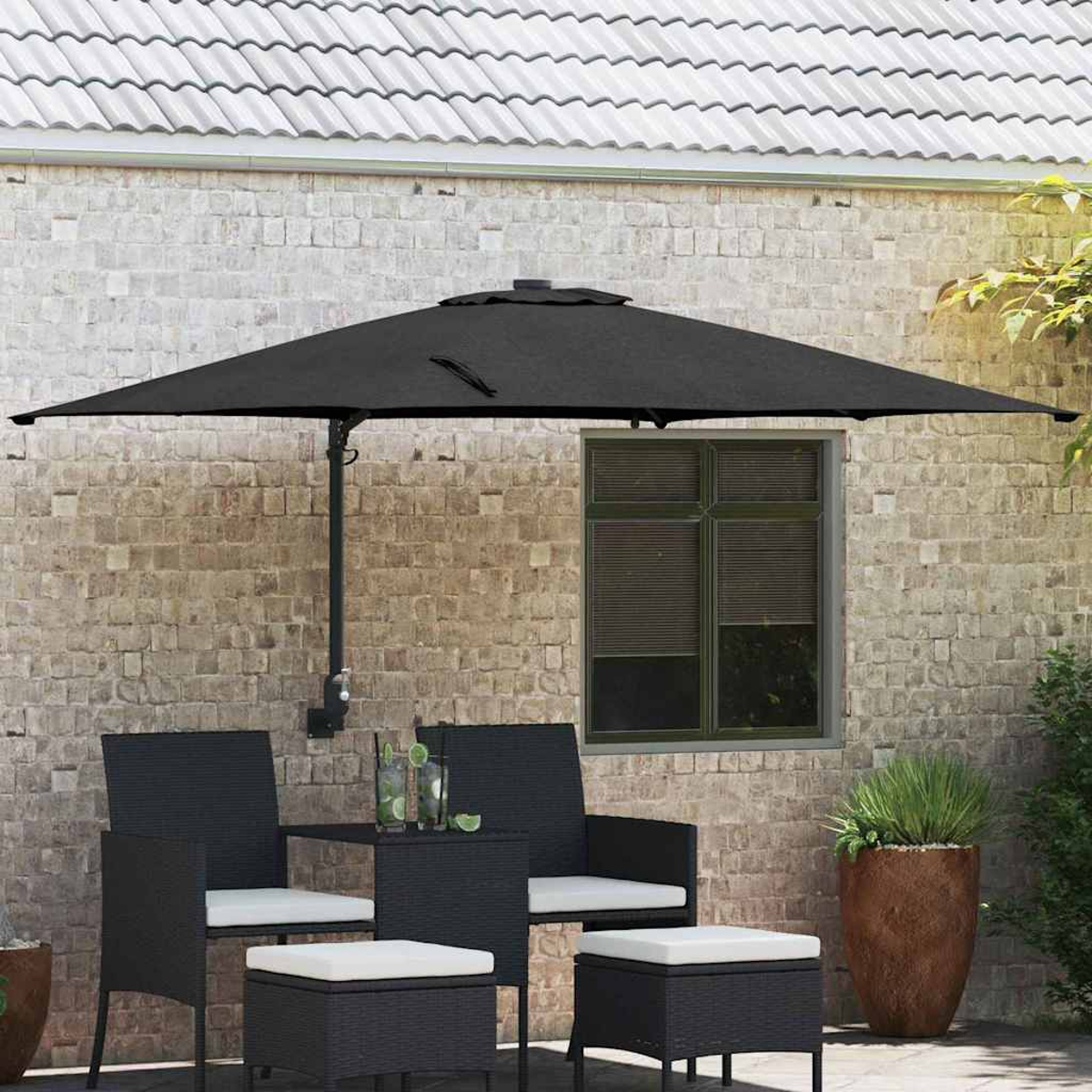 Scena all'aperto con mobili da patio neri, un ombrellone nero e un muro di mattoni. Sono visibili anche bevande e una pianta in vaso.