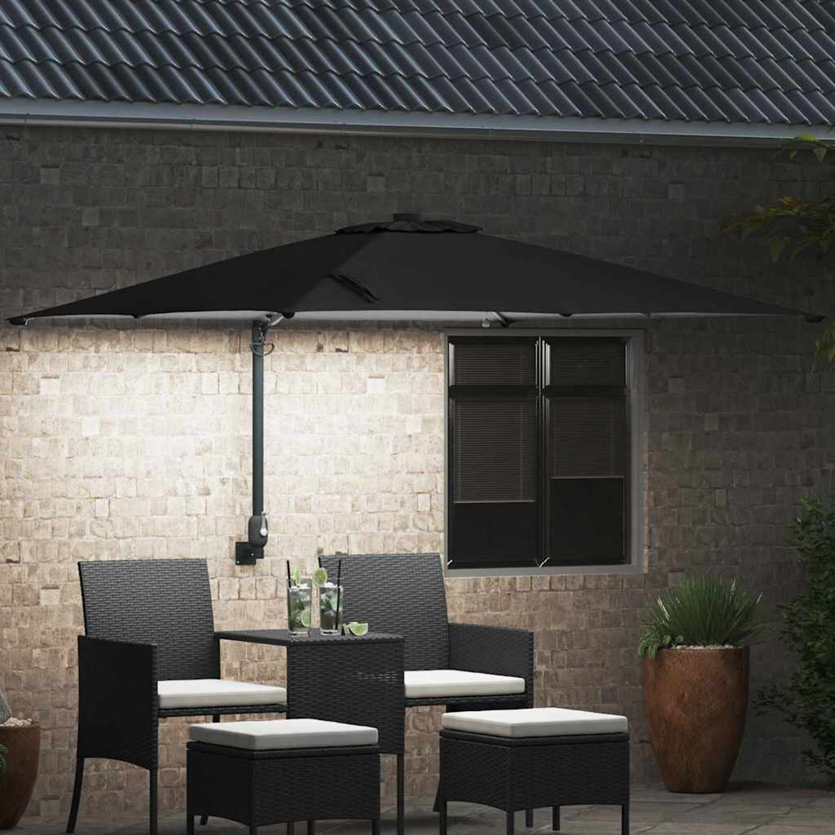 Patio all'aperto con ombrellone nero, sedie, tavolo e pouf. Bevande sul tavolo. Muro di mattoni e finestra sullo sfondo.