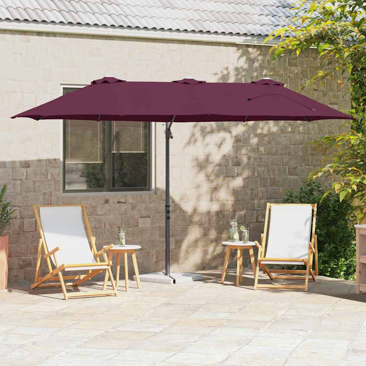 Una scena del patio con un grande ombrello bordeaux, due sedie, tavolini, bevande e un muro di mattoni sullo sfondo.