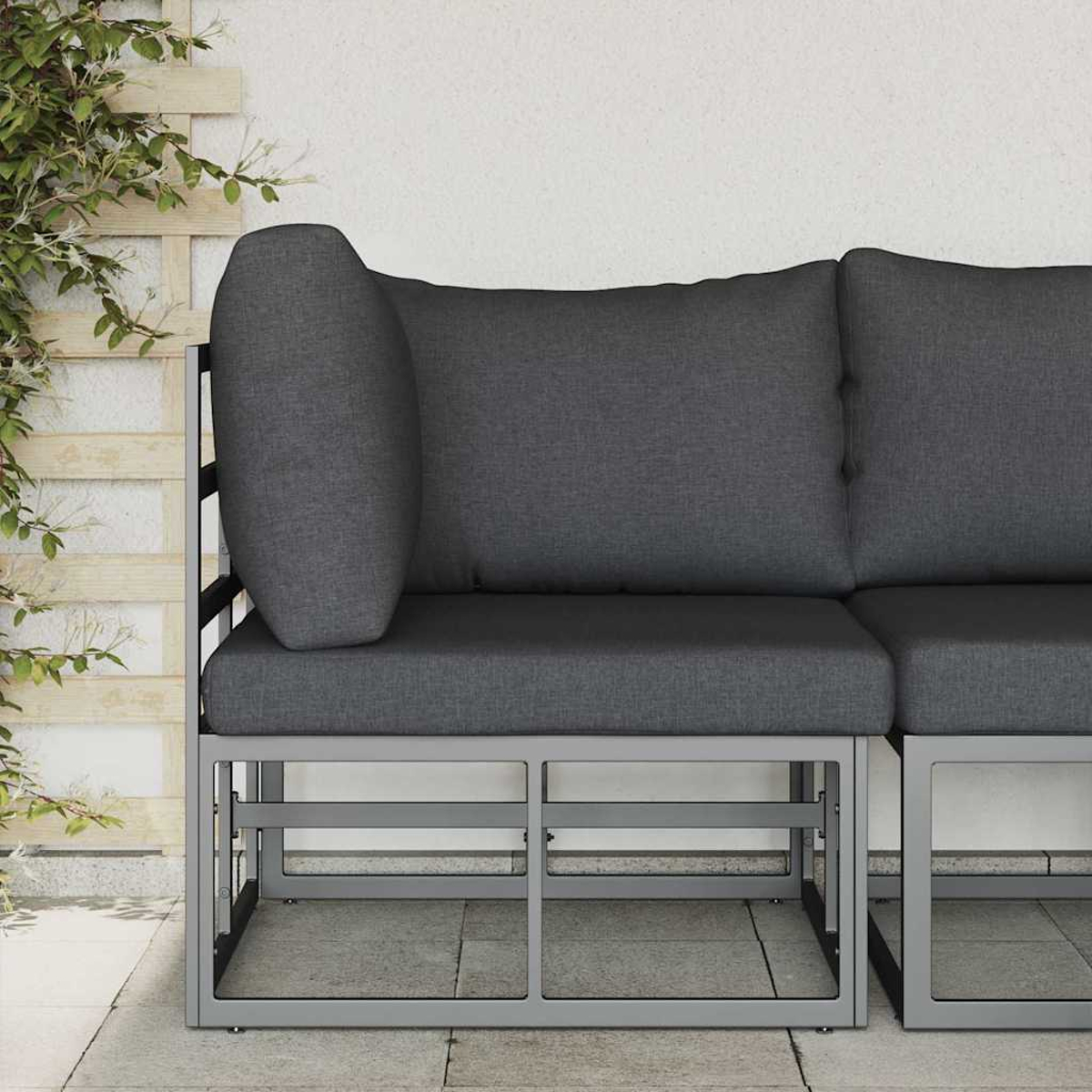 Un divano grigio da esterno con cuscini. È su un patio in pietra, con un traliccio e una pianta rampicante a sinistra e un muro bianco.