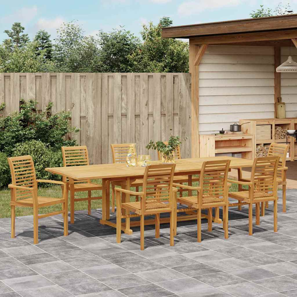 Essgruppe aus Holz im Freien: Tisch und Stühle. Auf Steinterrasse, mit Holzzaun und kleinem Küchenbereich.