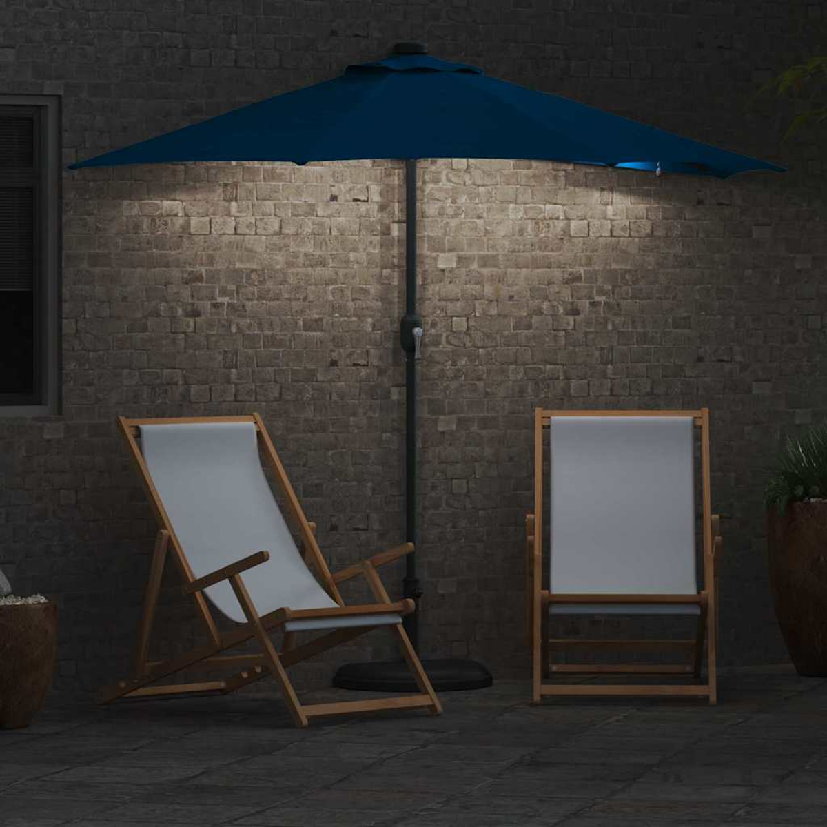 Due sedie in tela bianca con ombrellone blu illuminate da un muro di mattoni di notte. La scena evoca relax e comfort.