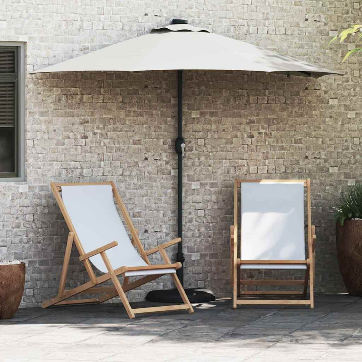 Due sedie a sdraio in tela bianca sotto un ombrello beige su un patio. Un muro di mattoni sullo sfondo con una pianta in vaso a destra.