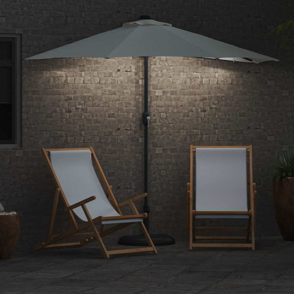 Scena all'aperto con due sedie, un ombrellone illuminato e un muro di mattoni sullo sfondo. Un vaso con una pianta a destra.