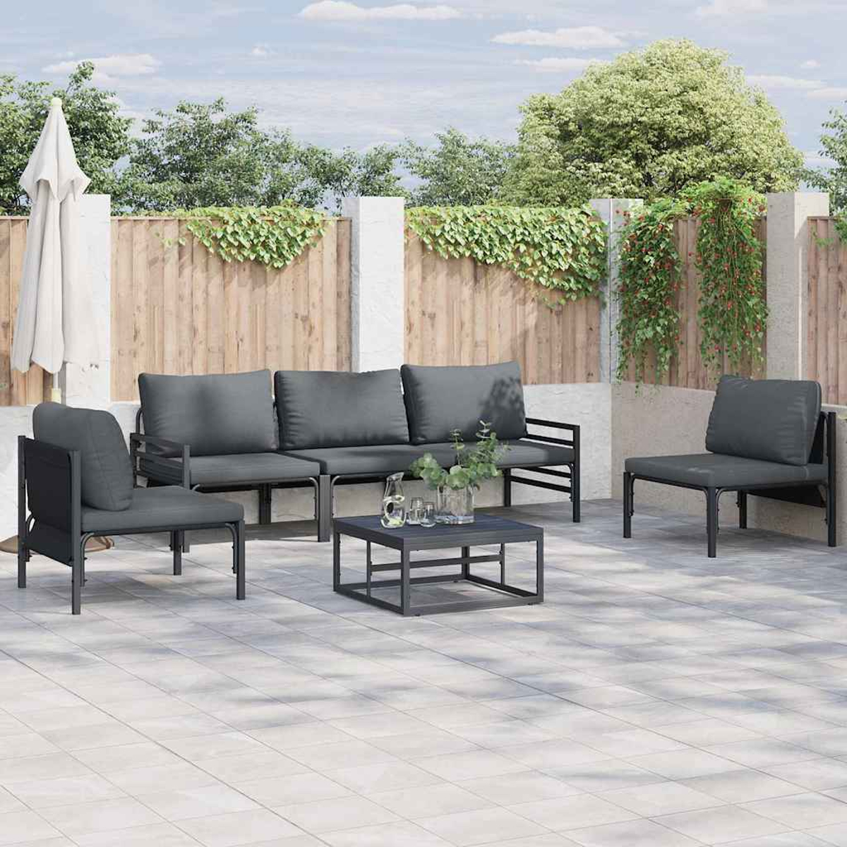 Terrassengarnitur mit grauen Kissen. Beinhaltet ein Sofa, zwei Sessel, einen Couchtisch und einen weißen Sonnenschirm vor einem Holzzaun.