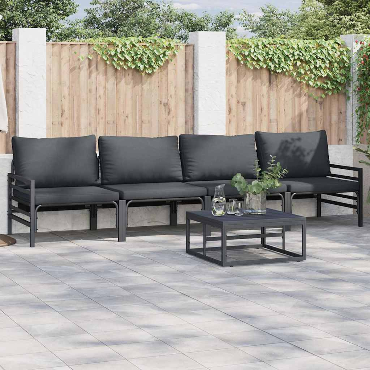 Szene im Freien mit grau gepolsterten Sitzmöbeln und einem kleinen Tisch. Efeu bedeckter Zaun im Hintergrund. Gepflasterte Terrasse.