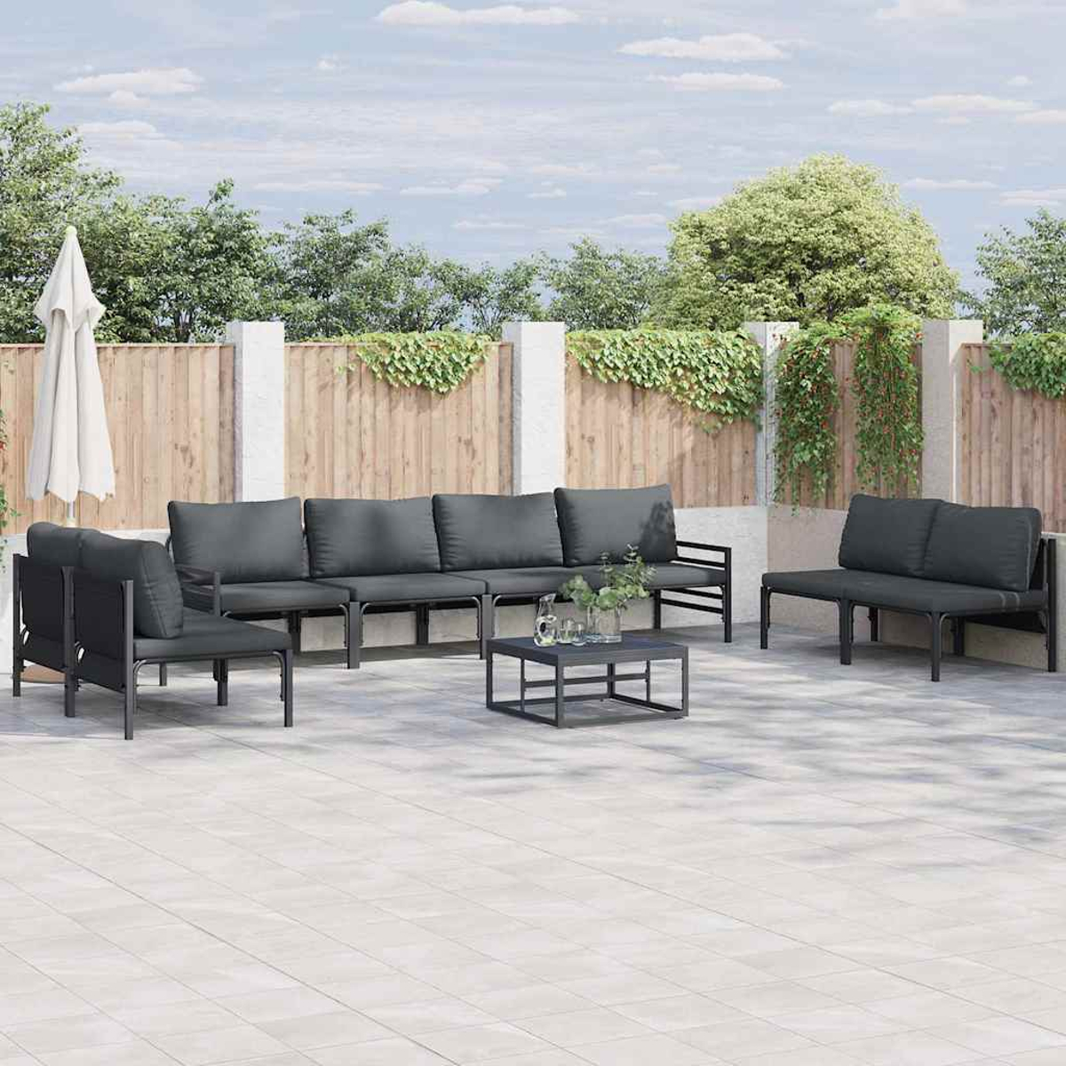 Garten-Sitzgruppe mit grauen Kissen auf einer Terrasse. Enthält ein Sofa, Stühle und einen Tisch. Im Hintergrund ein Zaun und Bäume.