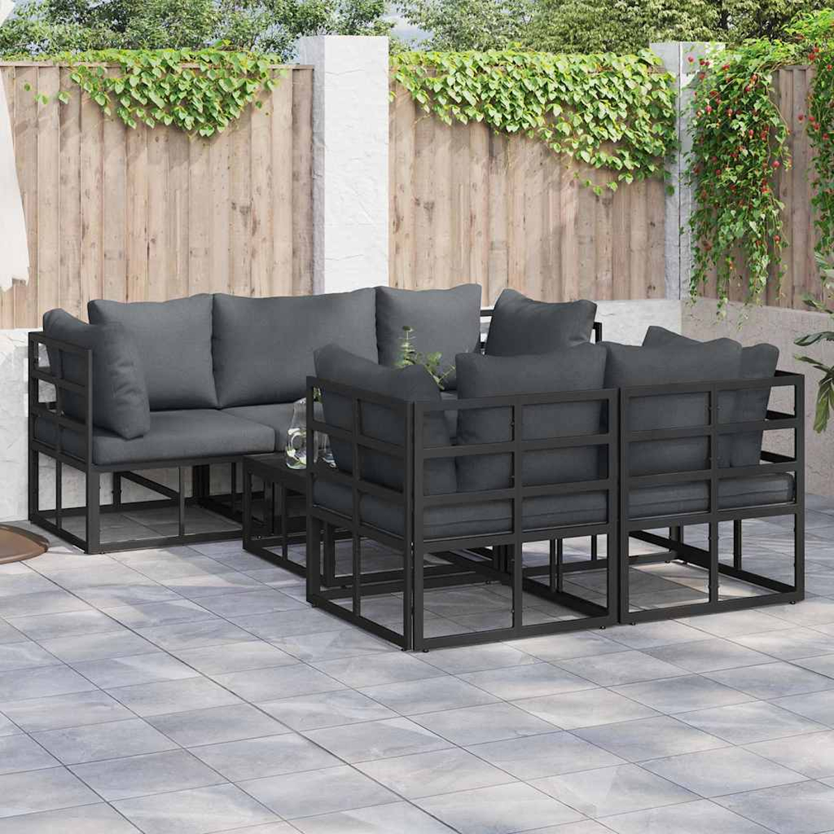 Conjunto de asientos para exteriores con cojines gris oscuro y marcos de metal negro. Incluye un sofá, dos sillas y una mesa pequeña, en un patio.