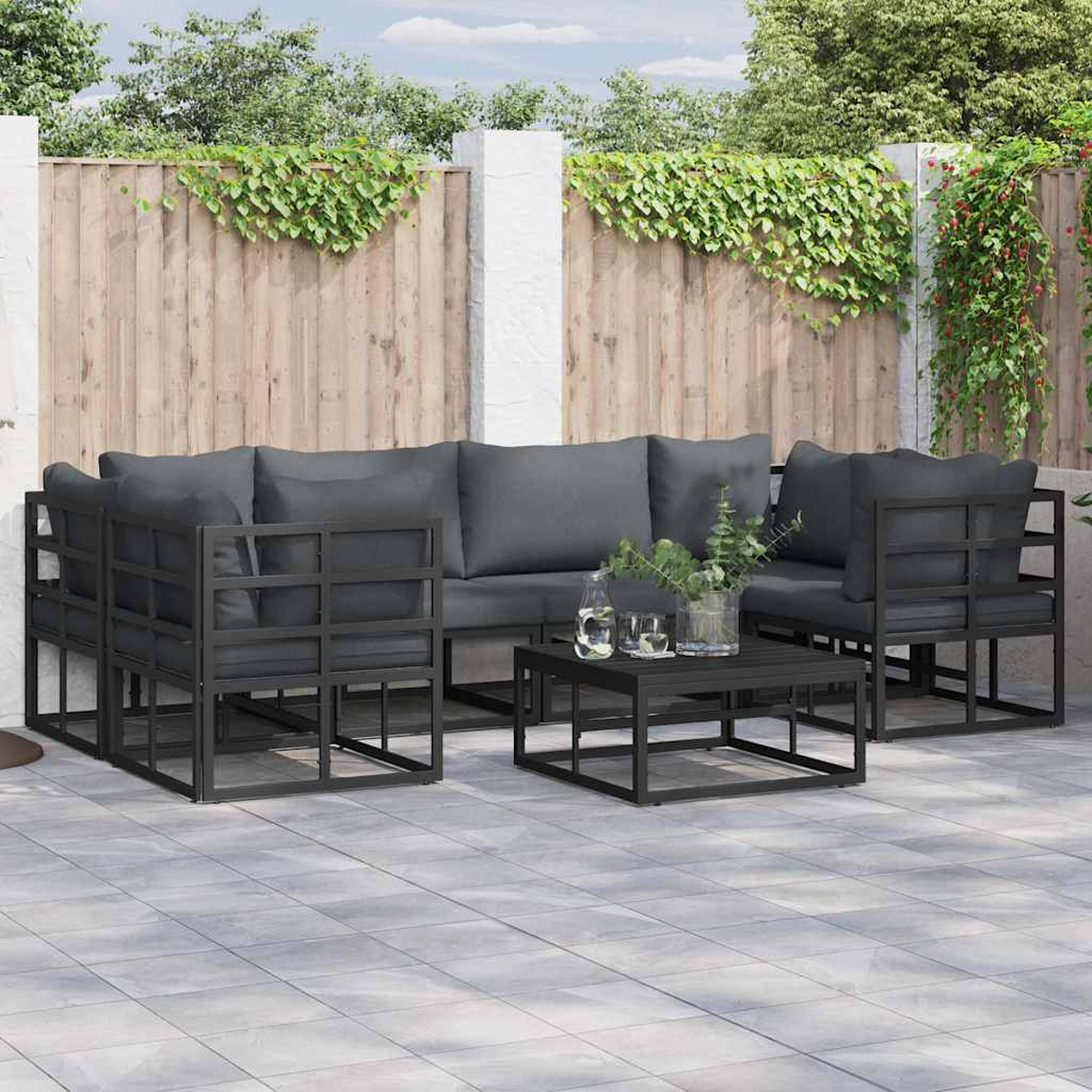Terrassengarnitur mit grauen Kissen, schwarzem Metallrahmen und einem quadratischen Couchtisch auf einer gefliesten Terrasse.