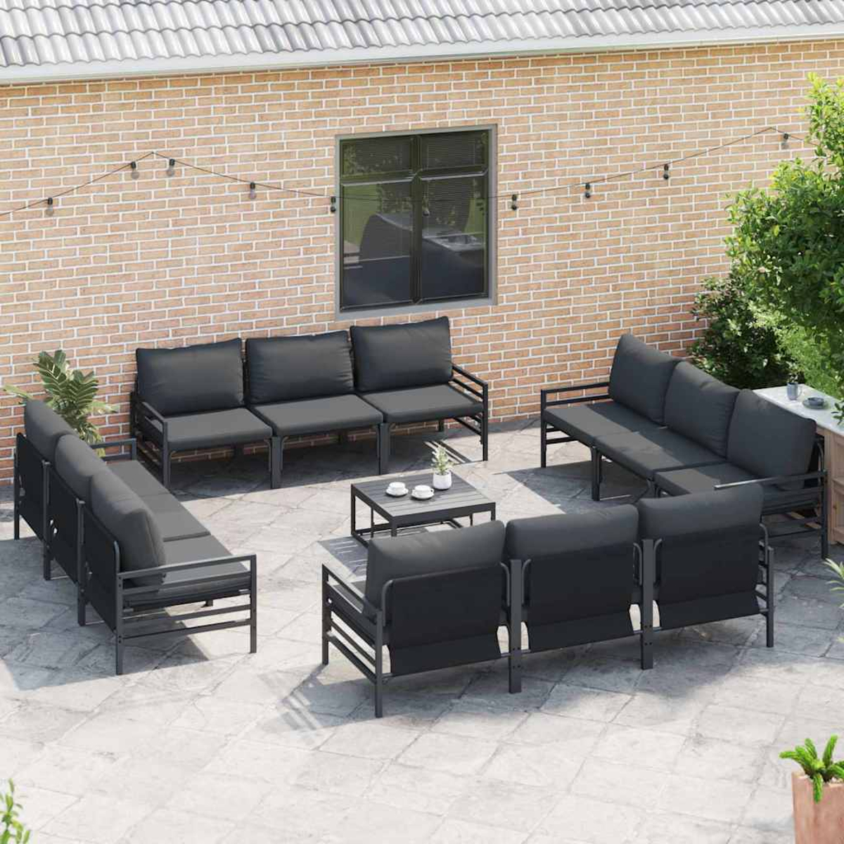 Terrassenset mit grauen Kissen und schwarzen Rahmen. Das Set umfasst Sofas, einen Couchtisch und eine Backsteinmauer im Hintergrund.