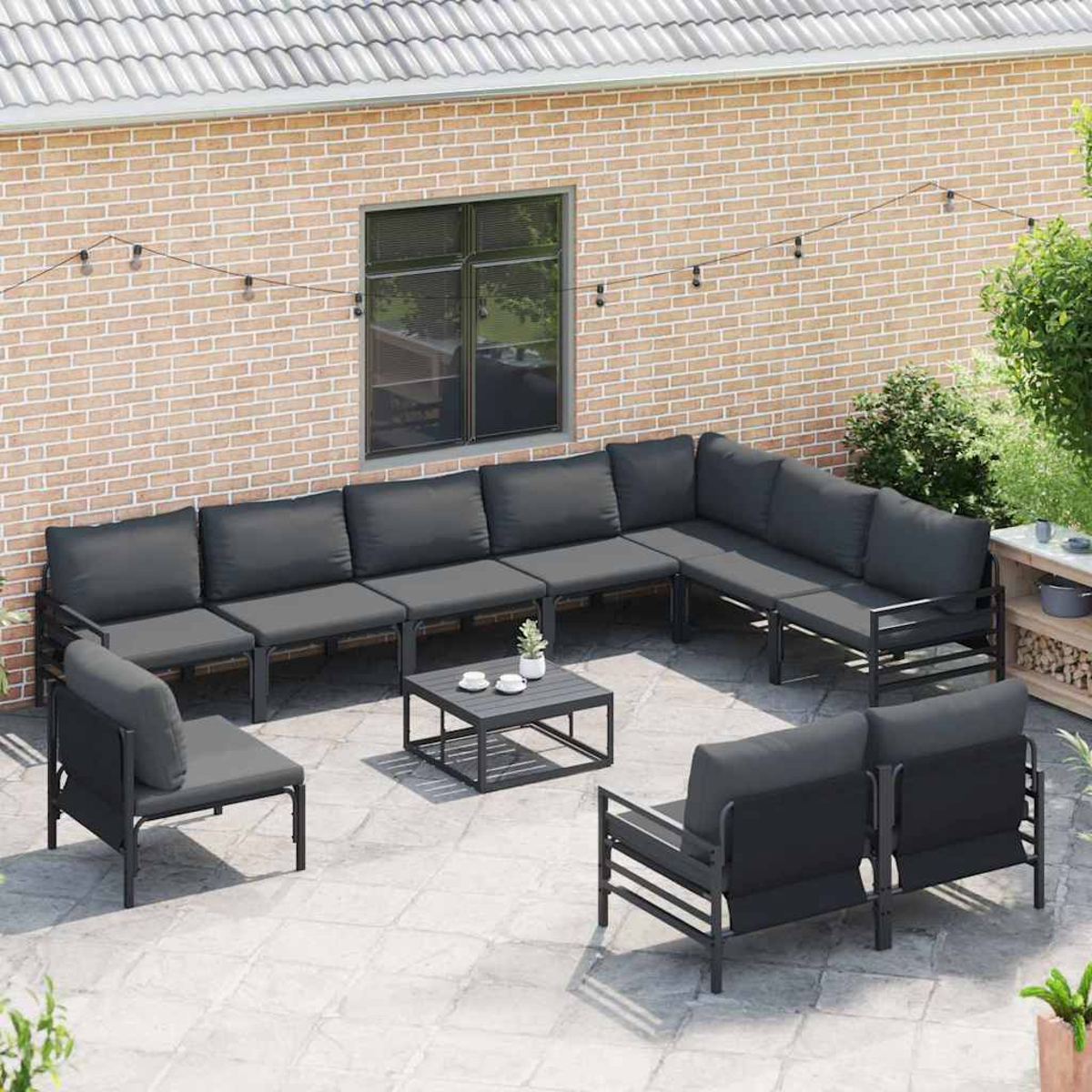 Gartenmöbel-Set auf einer Steinterrasse. Enthält Ecksofa, Sessel, Couchtisch und Backsteinmauer als Hintergrund.