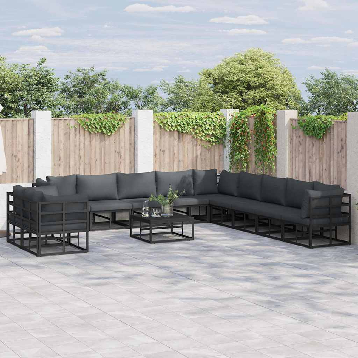 Ein Outdoor-Terrassenset mit dunkelgrauen Kissen steht auf einer gefliesten Terrasse. Im Hintergrund ist ein Holzzaun mit Grün.
