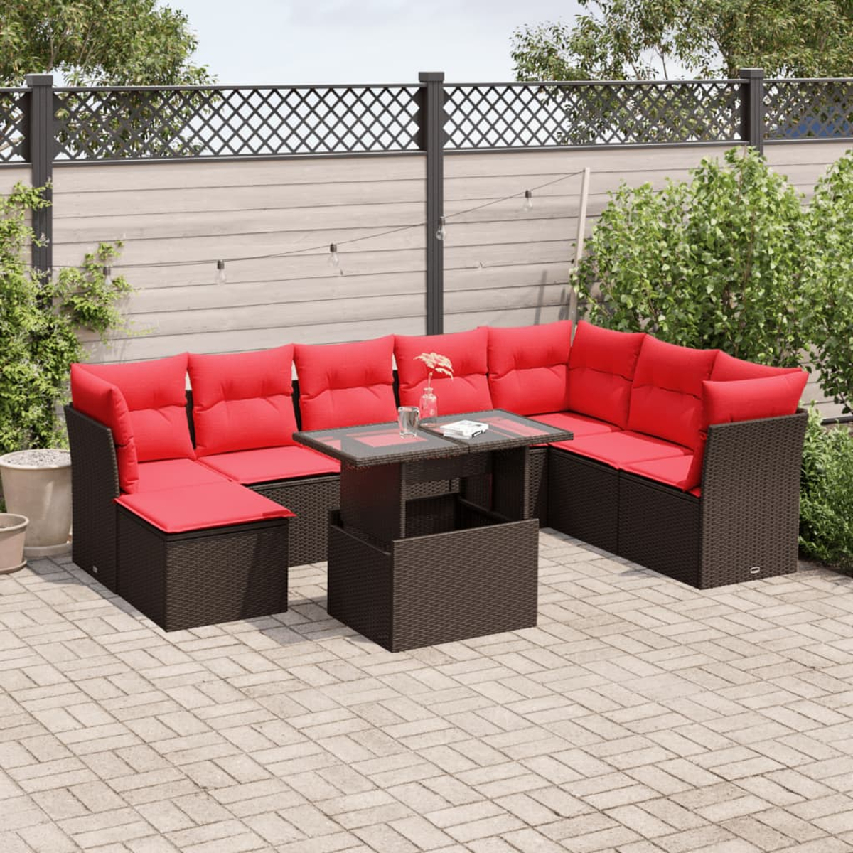 Outdoor-Ecksofa mit roten Kissen und Couchtisch auf einer Terrasse. Hintergrund sind ein Zaun und Grün.