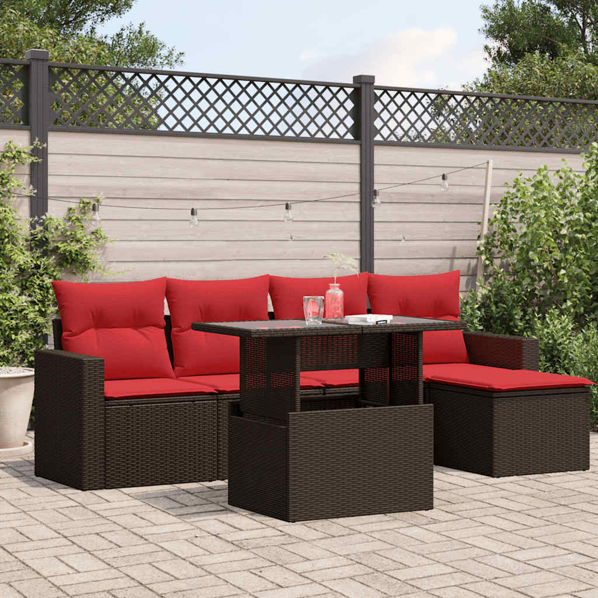 Garten-Terrassenset mit roten Kissen, Tisch und Zaun. Auf dem Tisch stehen ein Wasserglas und eine Flasche.