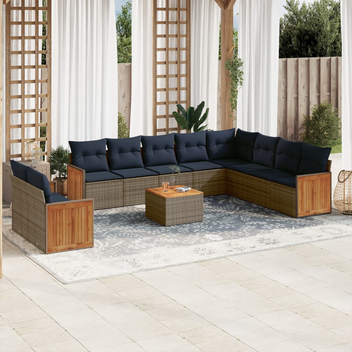 Outdoor-Ecksofa mit marineblauen Kissen, einem quadratischen Couchtisch und einem Teppich auf einer Terrasse. Weiße Vorhänge und Pflanzen im Hintergrund.