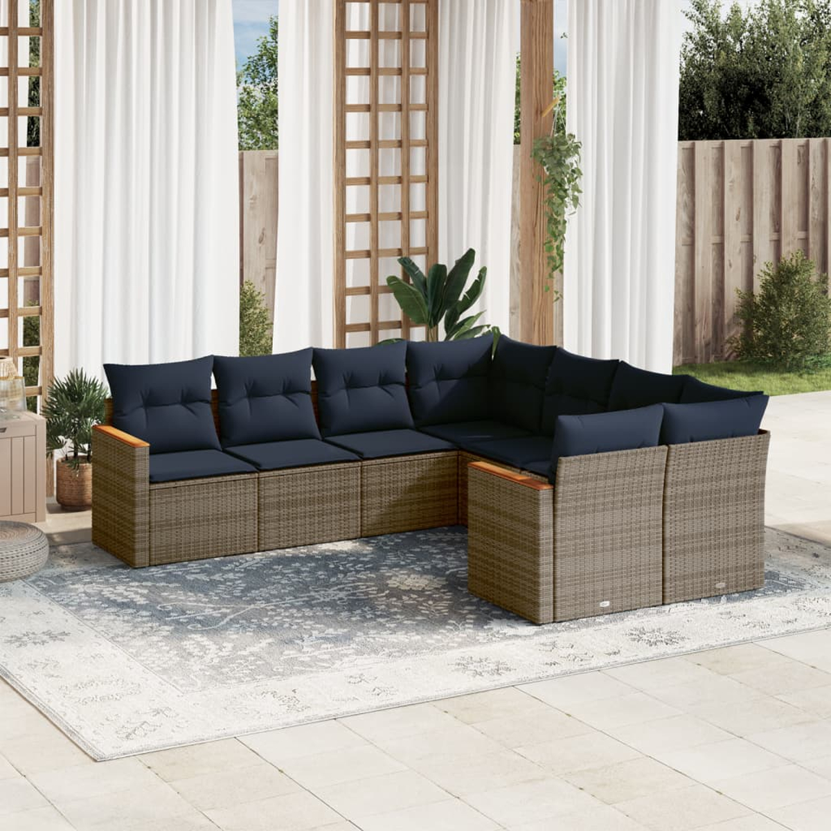 Outdoor-Ecksofa mit marineblauen Kissen auf einem gemusterten Teppich. Weiße Vorhänge im Hintergrund. Holzstruktur und Pflanzen.
