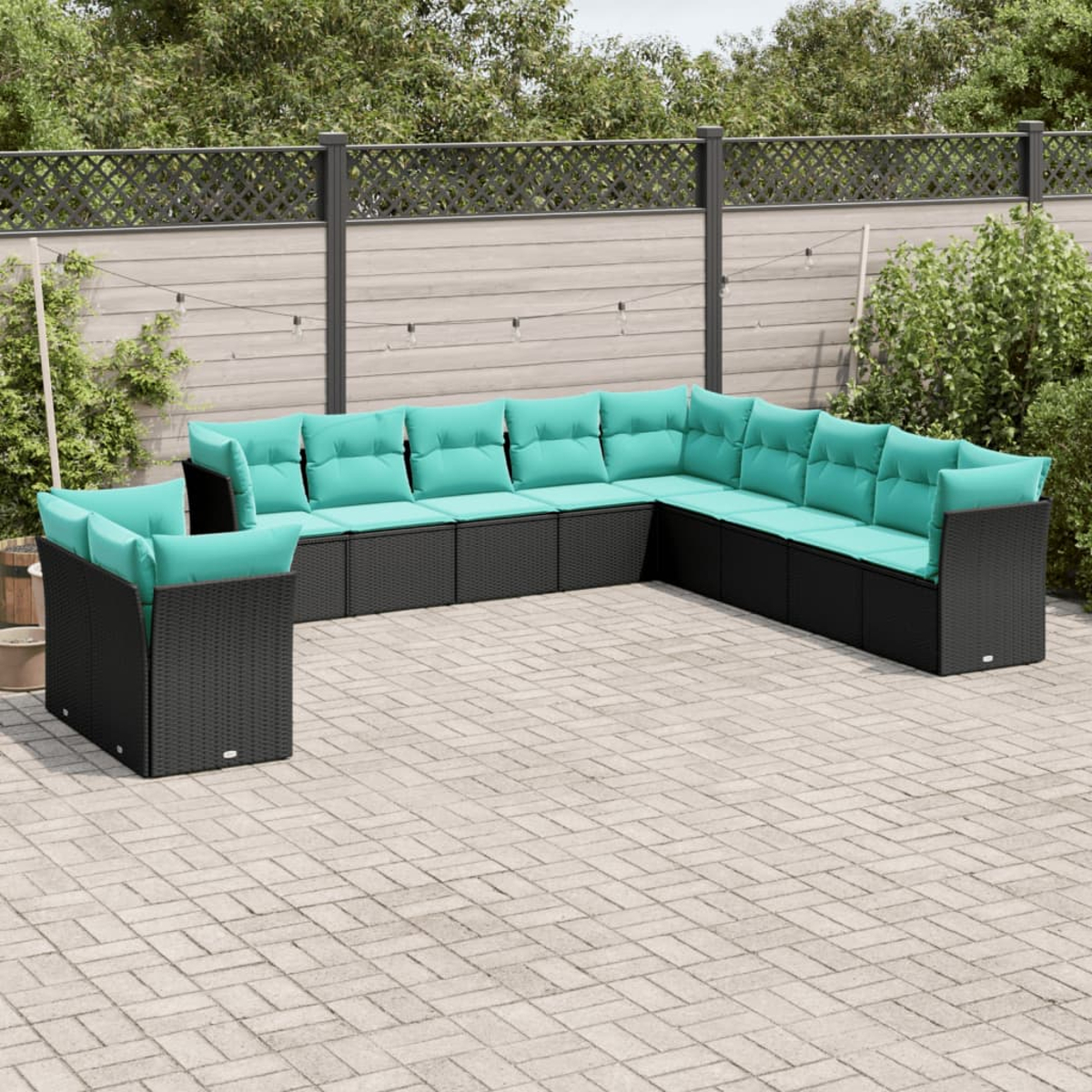 Outdoor-Ecksofa mit türkisfarbenen Kissen auf einer Steinterrasse. Schwarzer Korbrahmen, U-förmig angeordnet, vor einem Zaun und Grün.