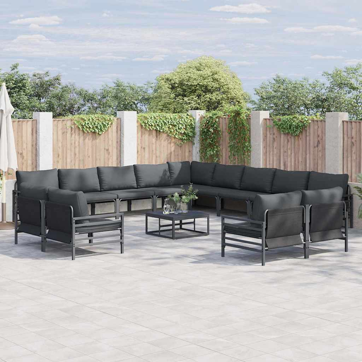 Outdoor-Sitzgruppe mit grauen Kissen auf einer Terrasse. Enthält ein Ecksofa, zwei Stühle und einen Couchtisch. Im Hintergrund ein Holzzaun.