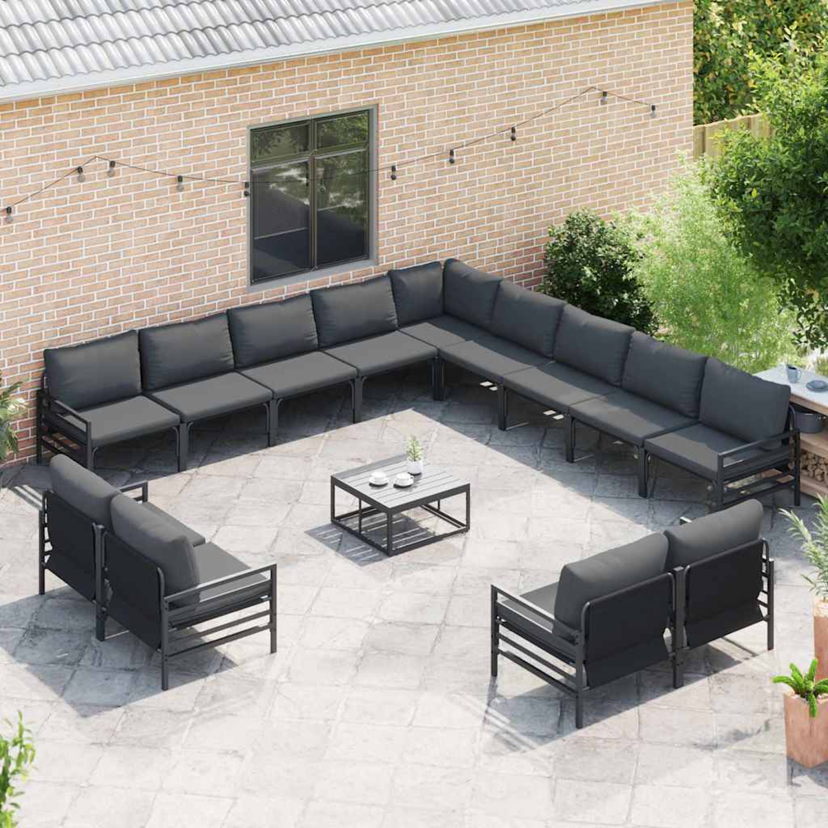 Szene auf der Terrasse mit grauen Sofas, die um einen kleinen Tisch angeordnet sind. Backsteinmauer im Hintergrund, Lichterketten und Topfpflanzen.