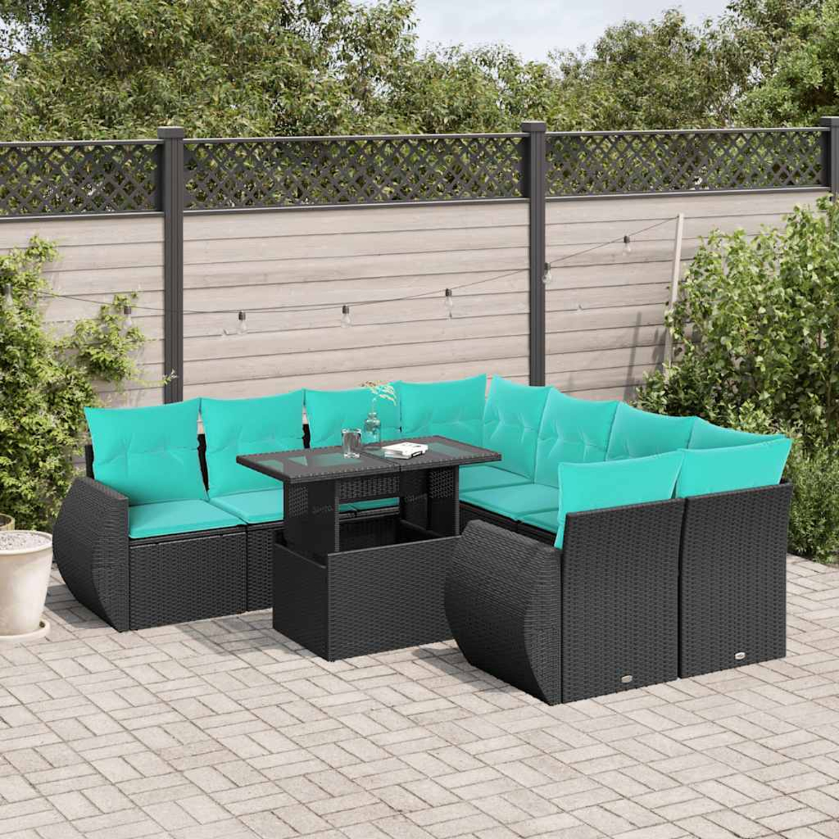 Garten-Sitzgruppe mit schwarzem Korbmöbel und türkisfarbenen Kissen. Ein Tisch mit Glasplatte steht vor dem Sofa. Im Hintergrund ein Zaun und Pflanzen.