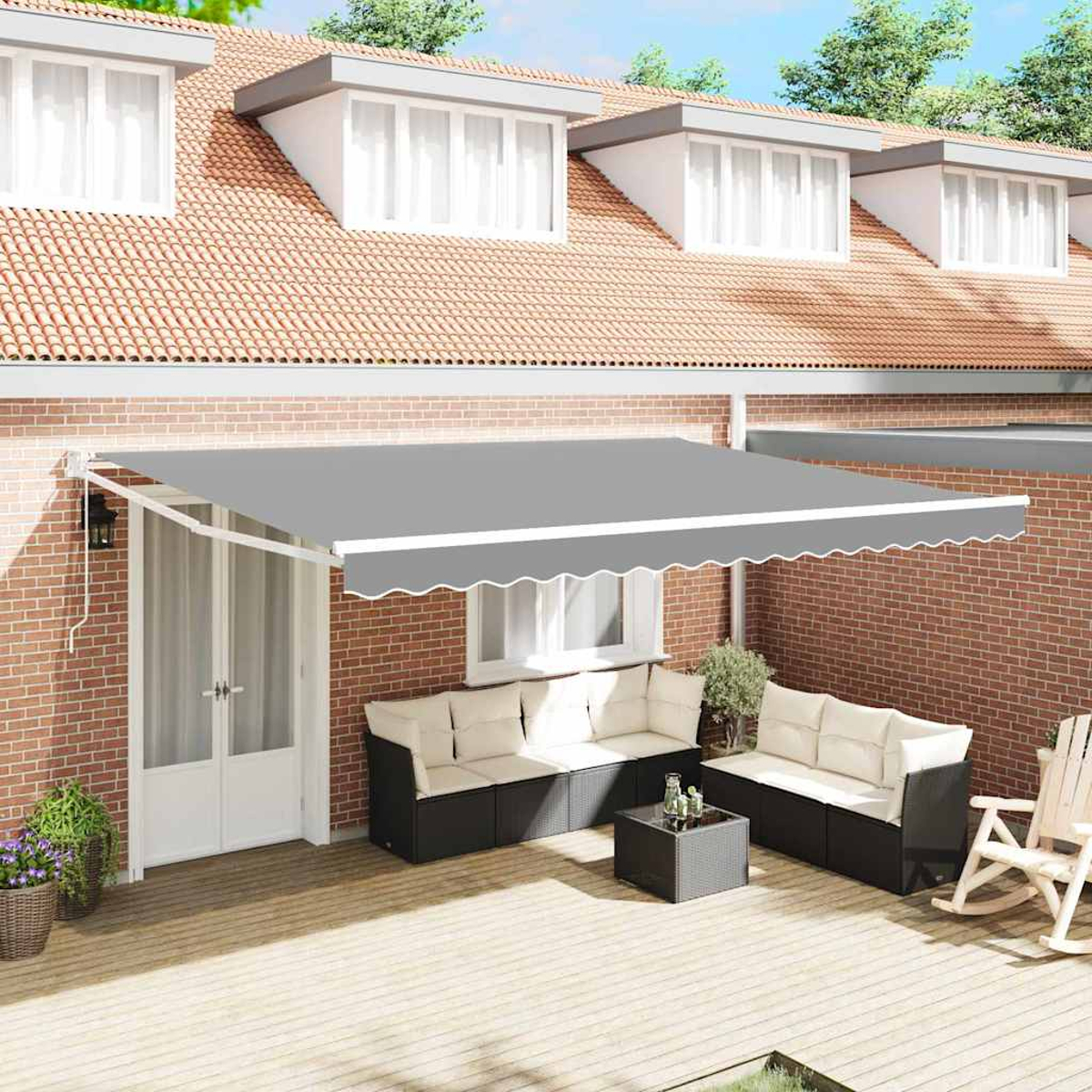 Terrasse im Freien mit grauem Markise, Sitzgelegenheiten und roter Backsteinmauer. Ein Holzdeck und ein Haus sind im Hintergrund.