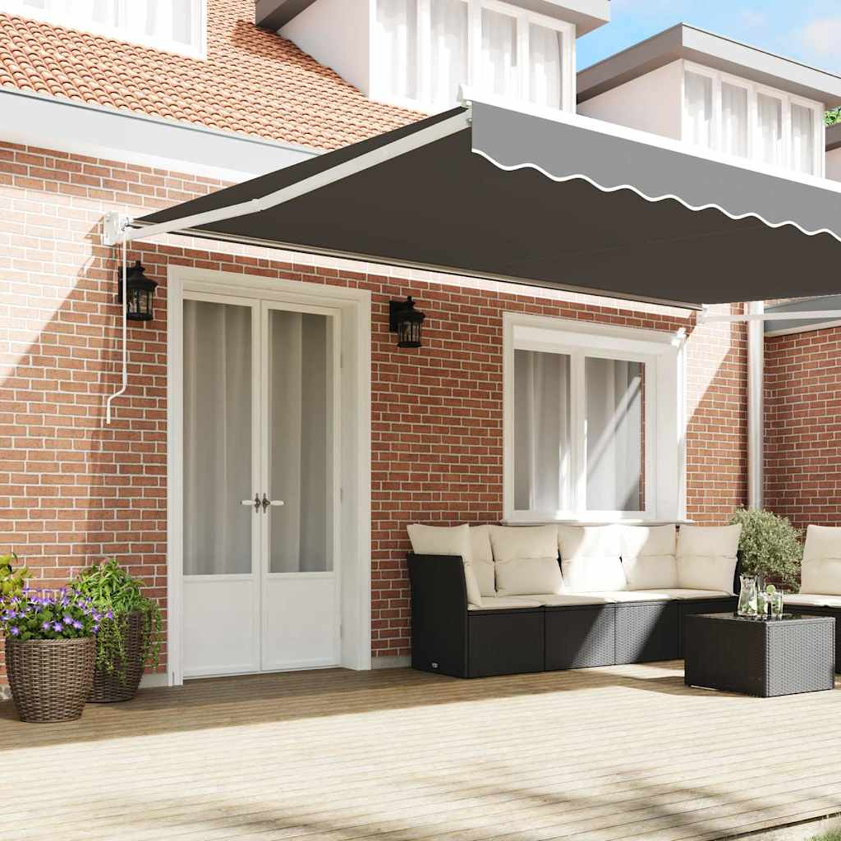 Eine Terrasse mit dunkler grauer Markise, weißer Tür, schwarzem Sofa mit Kissen und Topfpflanzen vor einer Backsteinmauer.