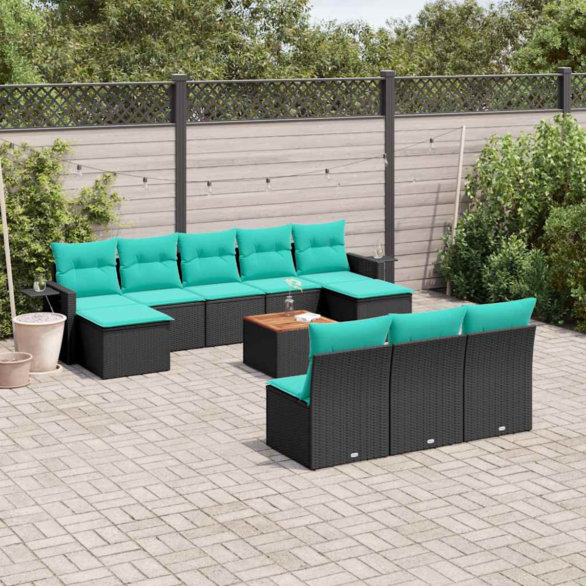 Garten-Sitzgruppe. Schwarze Korbmöbel mit türkisfarbenen Kissen. Couchtisch aus Holz. Gepflasterte Terrasse mit Zaun und Grün im Hintergrund.