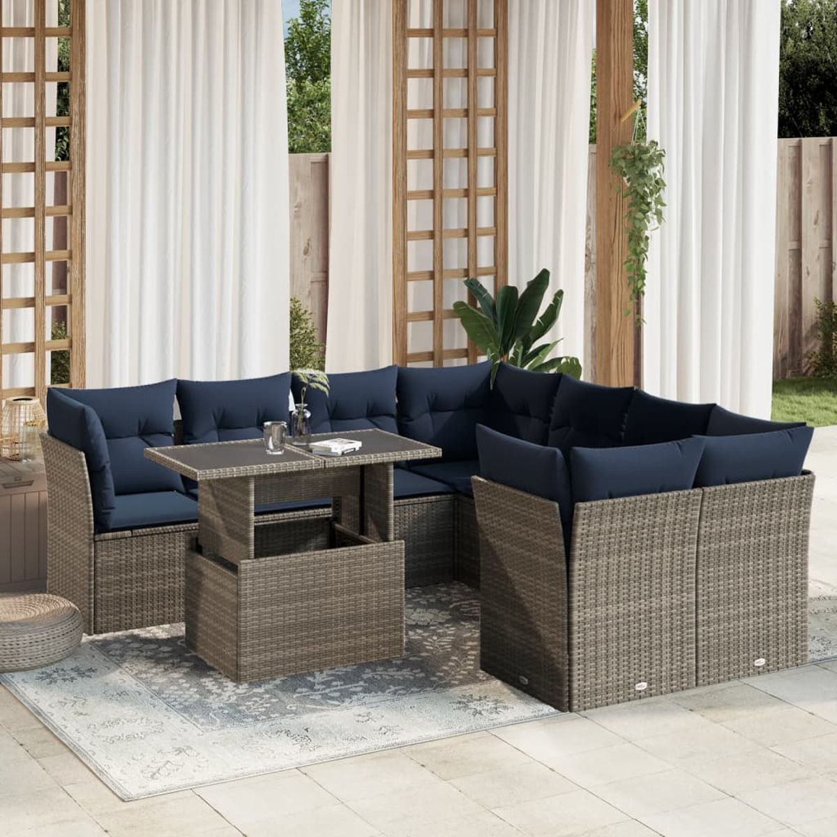 Outdoor-Sitzgruppe mit blauen Kissen, Gestellen im Rattan-Stil und einem Tisch auf einem Teppich. Transparente Vorhänge und Grün im Hintergrund.