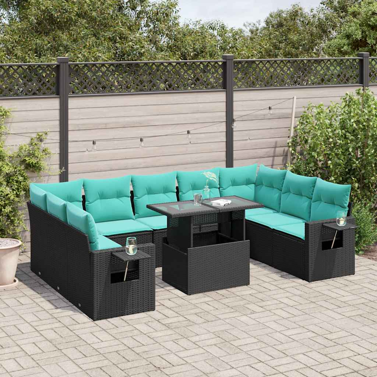 Outdoor-Ecksofa mit türkisfarbenen Kissen und schwarzem Korbgewebe, Glastisch, auf einer Ziegelterrasse, vor Holzzaun.