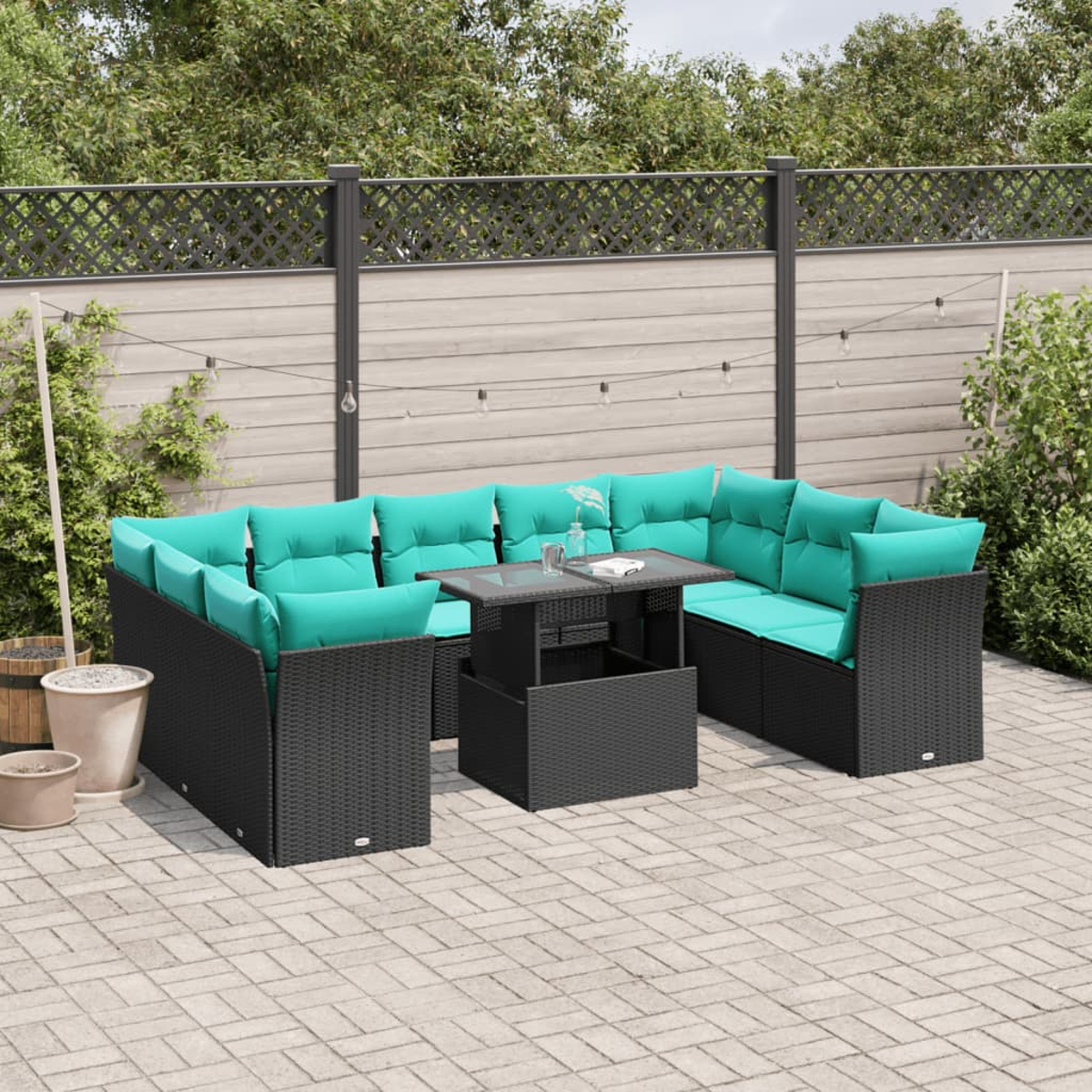 Outdoor-Ecksofa mit türkisfarbenen Kissen und schwarzem Korbgeweberahmen. Glastisch und Backstein-Patio. Zaun und Grün im Hintergrund.