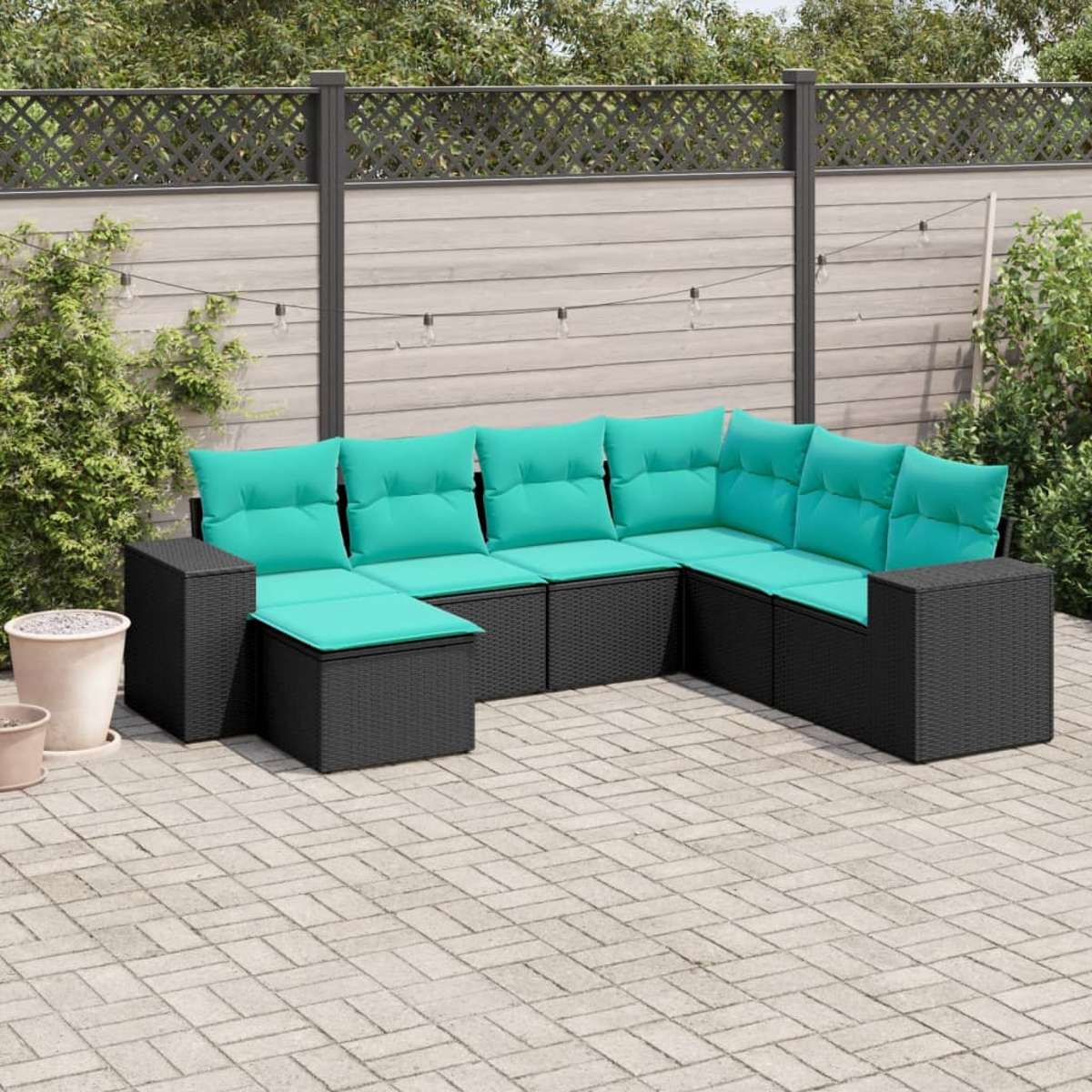 Un sofá seccional exterior con cojines turquesa está en un patio. El fondo incluye una cerca, plantas y luces de cadena.