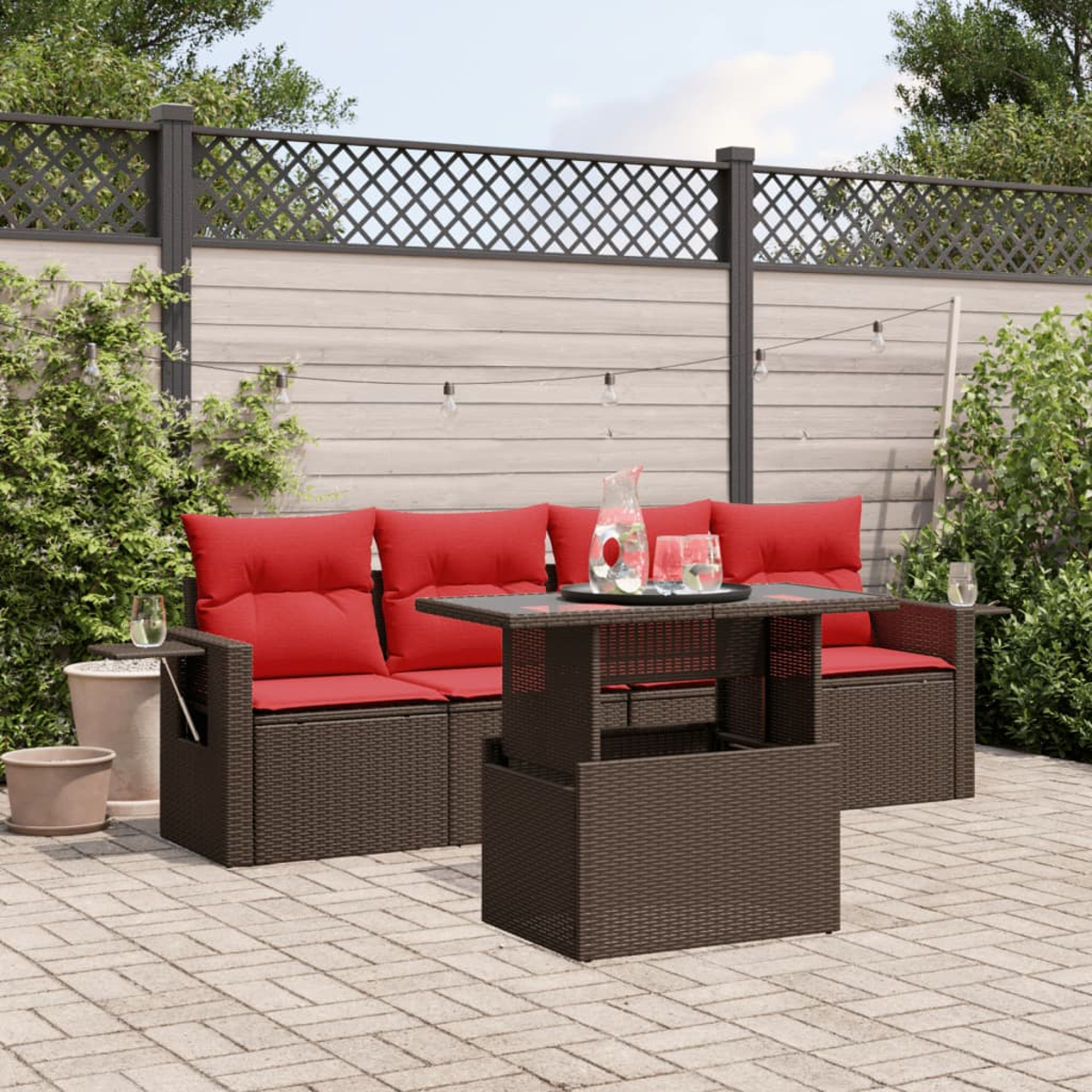 Terrassengarnitur mit roten Kissen. Ein Tisch mit Getränken steht vor dem Sofa. Ziegelpflaster und Holzzaun.