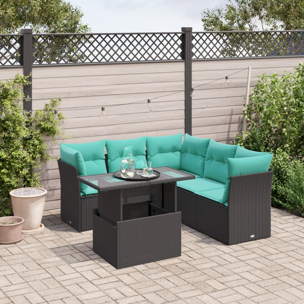 Garten-Sitzgruppe mit türkisfarbenen Kissen, einem Tisch mit Glasplatte und Getränken. Auf einer Ziegelterrasse mit Holzzaun im Hintergrund.