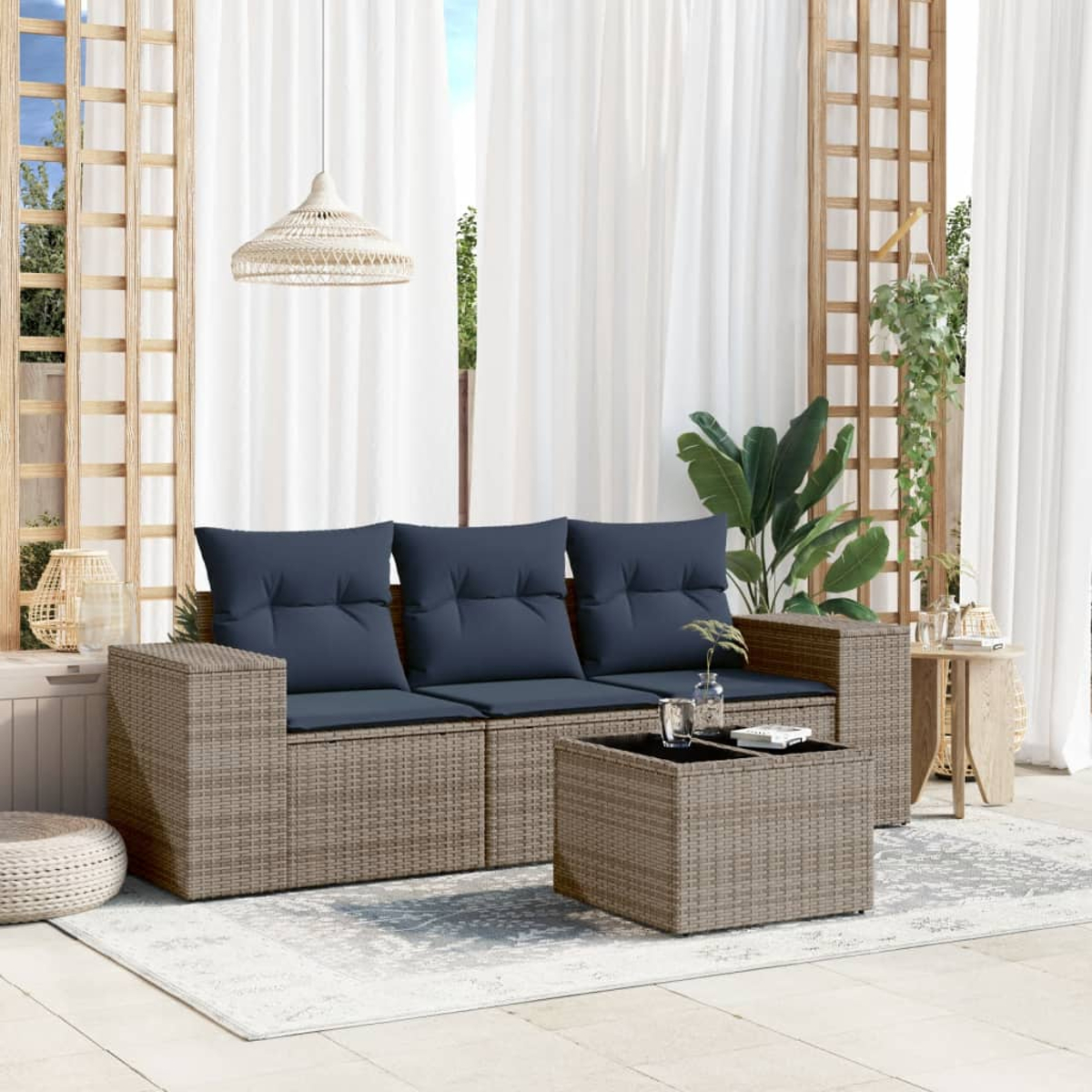 Terrasse mit grauem Korbssofa, dunkelblauen Kissen und einem passenden Couchtisch auf einem gemusterten Teppich. Weiße Vorhänge.