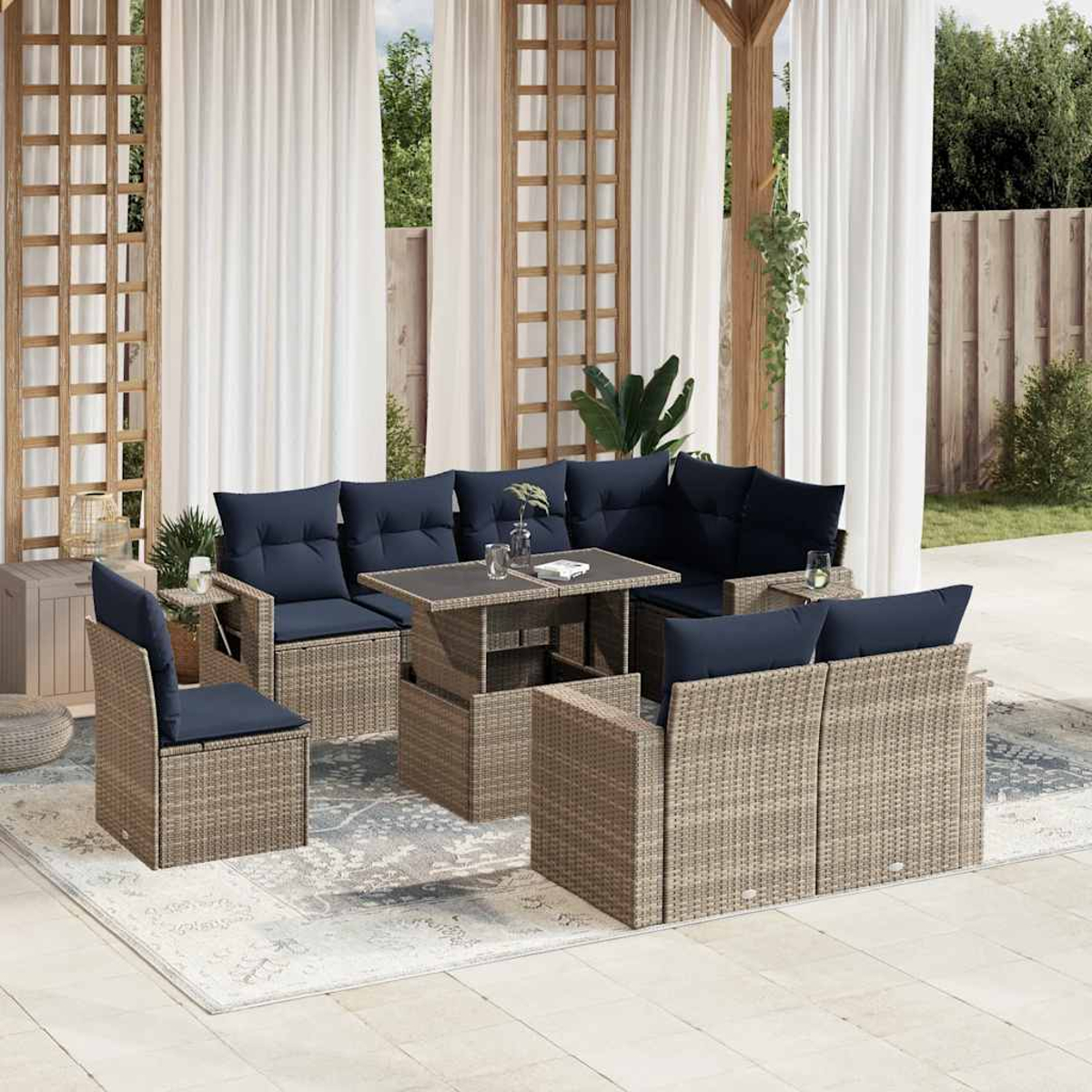 Gartenmöbel-Set aus Korbgeflecht mit marineblauen Kissen. Enthält Sofa, Stühle und Tisch auf einem gemusterten Teppich. Weiße Vorhänge und Grün im Hintergrund.