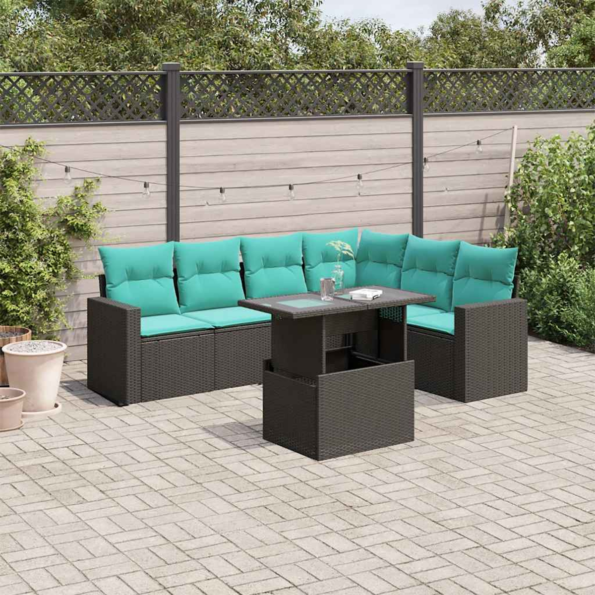 Garten-Sitzgruppe mit türkisfarbenen Kissen und einem Tisch. Auf einer gepflasterten Terrasse mit Holzzaun im Hintergrund.