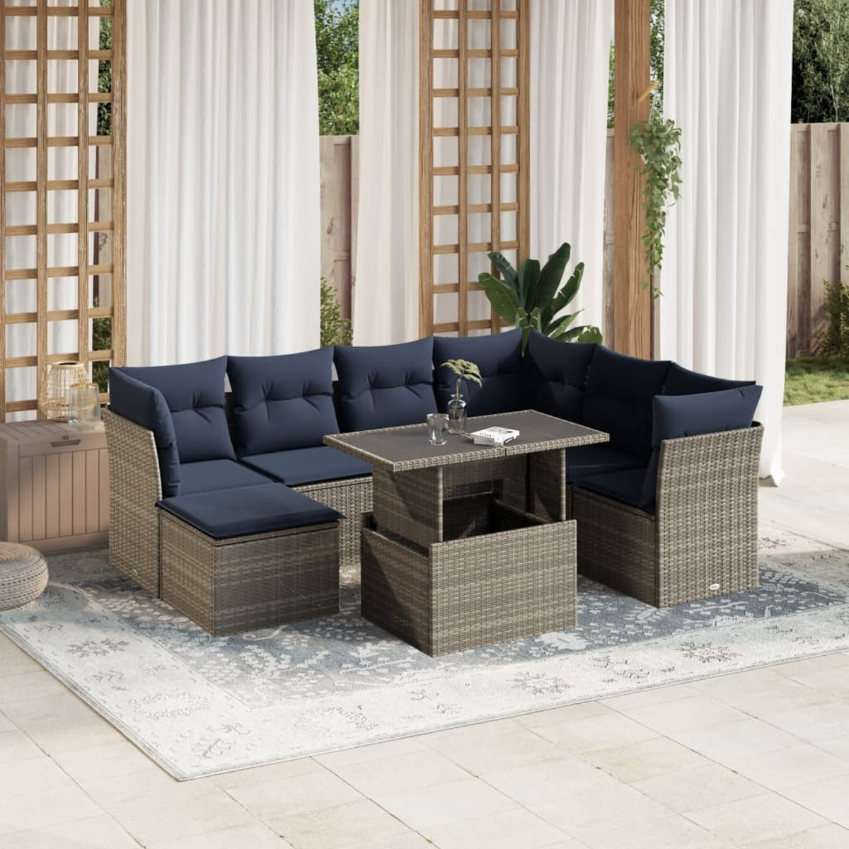 Sofá seccional para exteriores con cojines azul marino y mesa elevable. Sobre una alfombra, con cortinas blancas y fondo de celosía de madera.