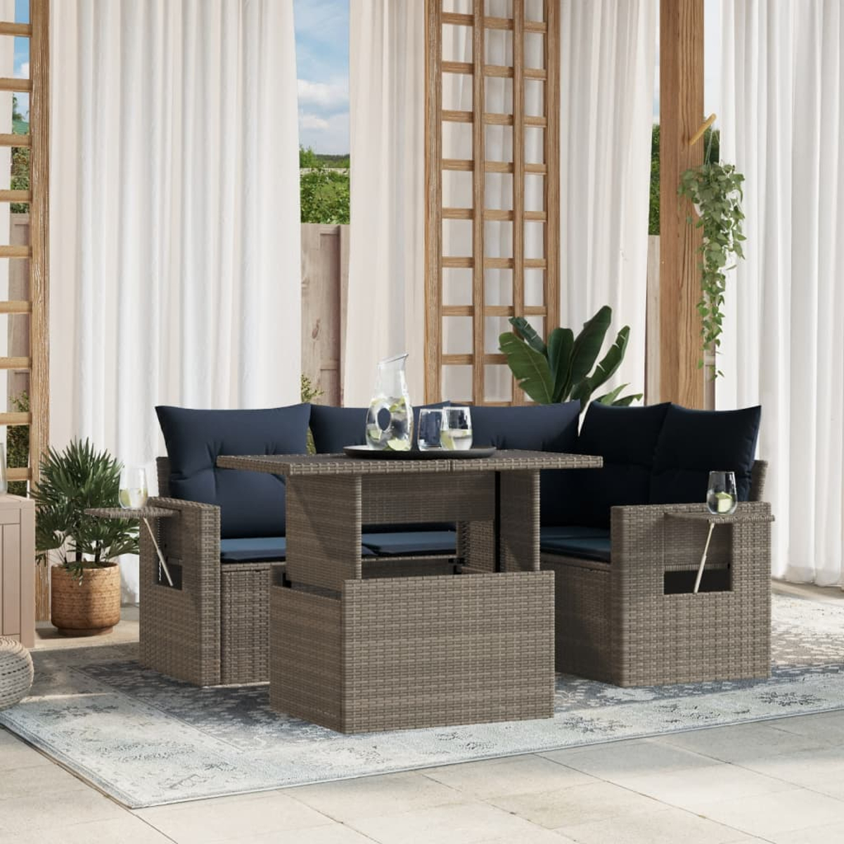 Terrassenset mit Rattanmöbeln, blauen Kissen und einem Tisch mit Hubfunktion. Enthält Pflanzen, Gläser und transparente weiße Vorhänge.