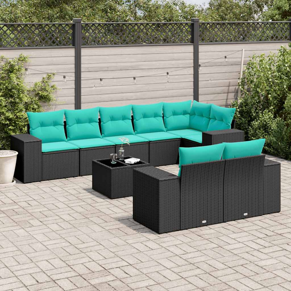 Gartenmöbel-Set mit schwarzem Korbgeflecht, türkisfarbenen Kissen und einem kleinen Tisch auf einer Backstein-Terrasse, im Hintergrund ein Zaun.