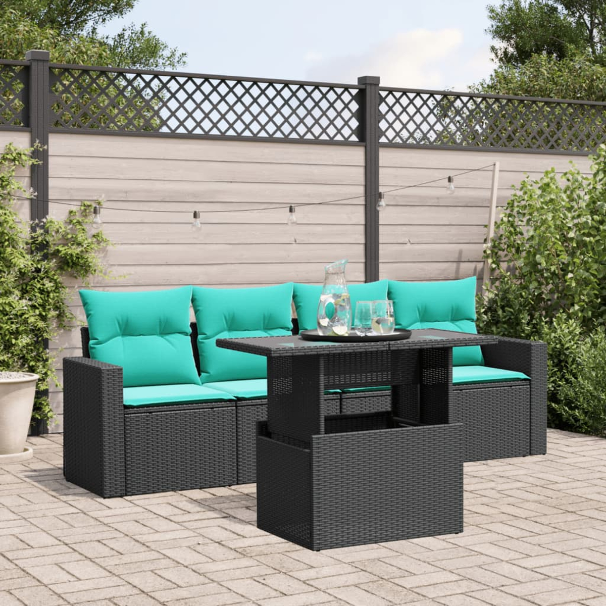 Gartenmöbel-Set mit schwarzem Korbmöbeln und türkisfarbenen Kissen, Tisch mit Wasser und Gläsern, vor Holzzaun.