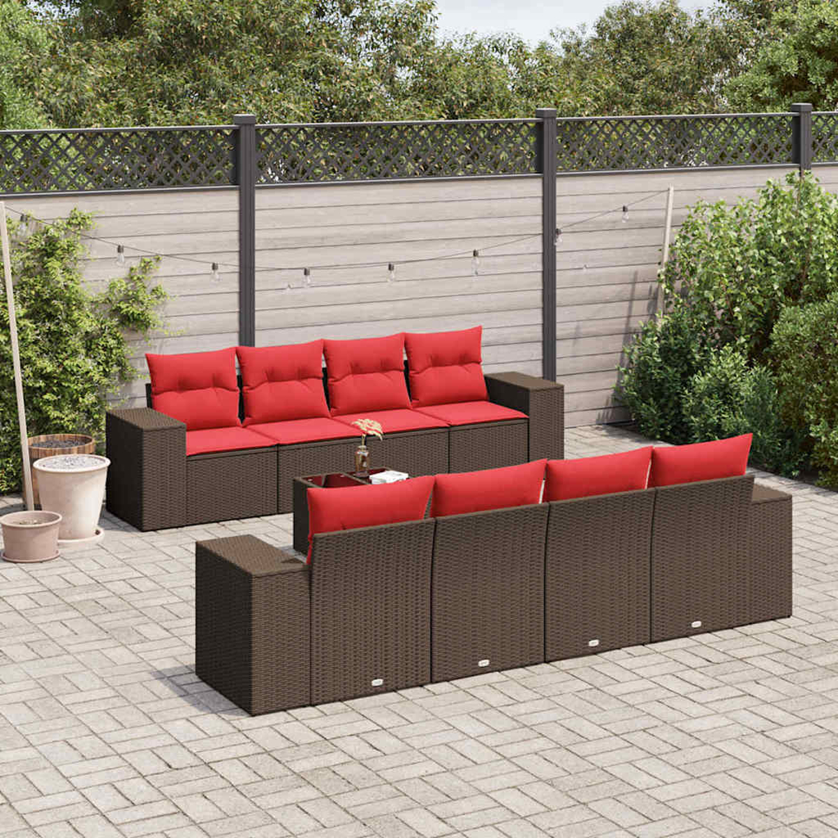 Garten-Set mit braunen Korbsitzgruppen, roten Kissen und einem Couchtisch mit Glasplatte. Auf einer Ziegelterrasse in der Nähe eines Zauns.