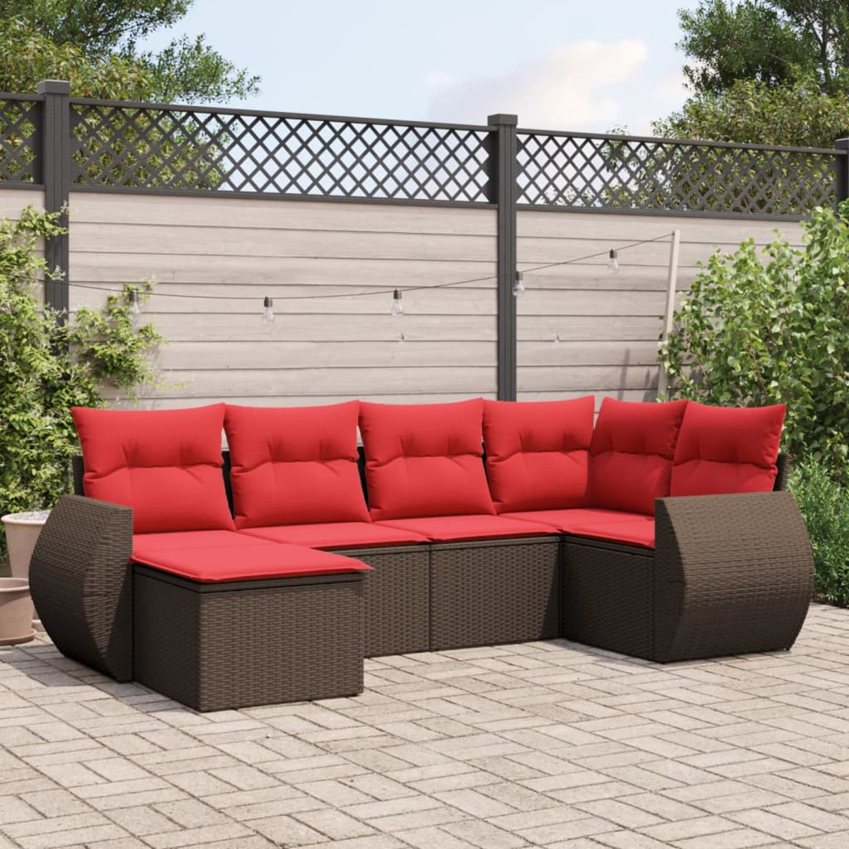 Outdoor-Ecksofa mit roten Kissen auf einer Terrasse. Zaun im Hintergrund, Lichterketten darüber.
