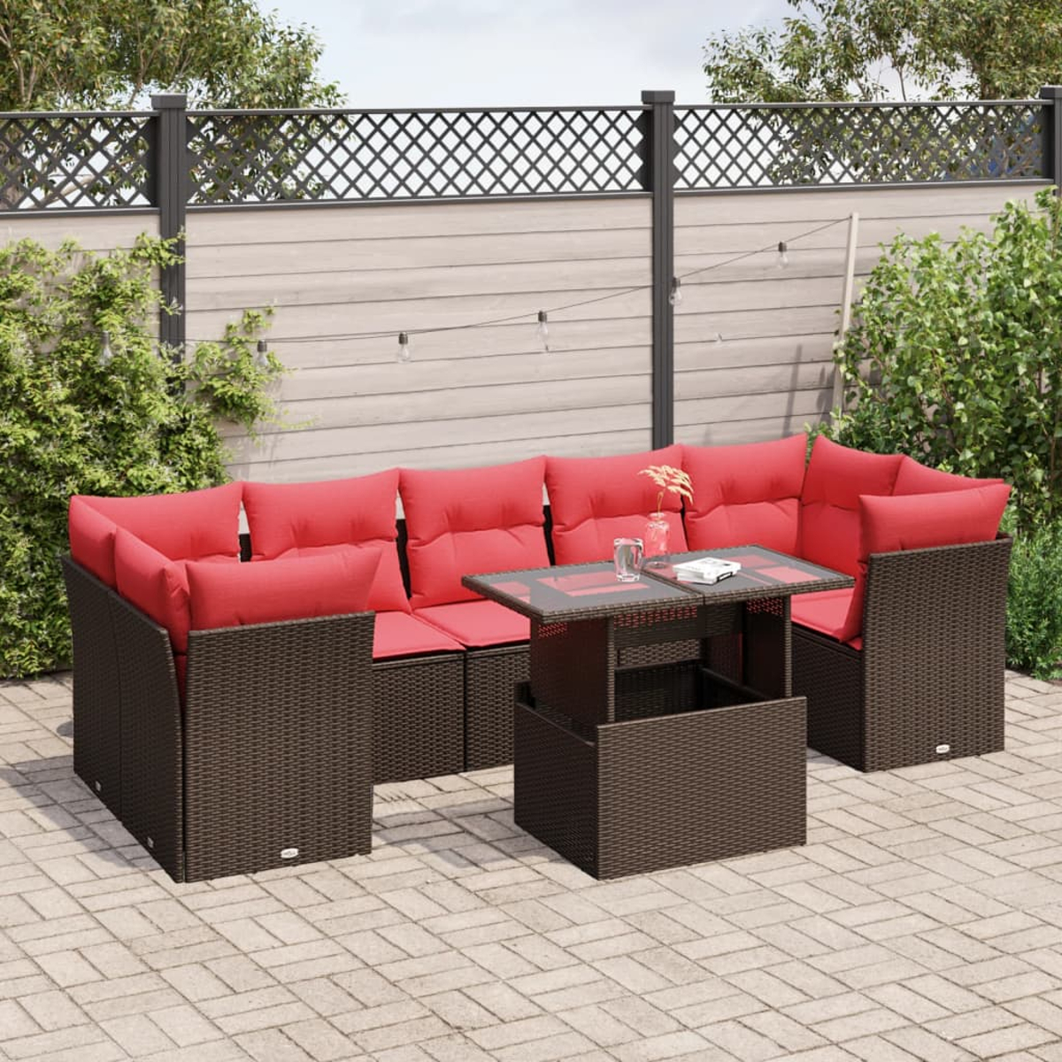 Gartenmöbel-Set mit rotem gepolsterten Ecksofa und einem Tisch mit Hubfunktion auf einer gepflasterten Terrasse. Im Hintergrund ein Zaun und Grün.
