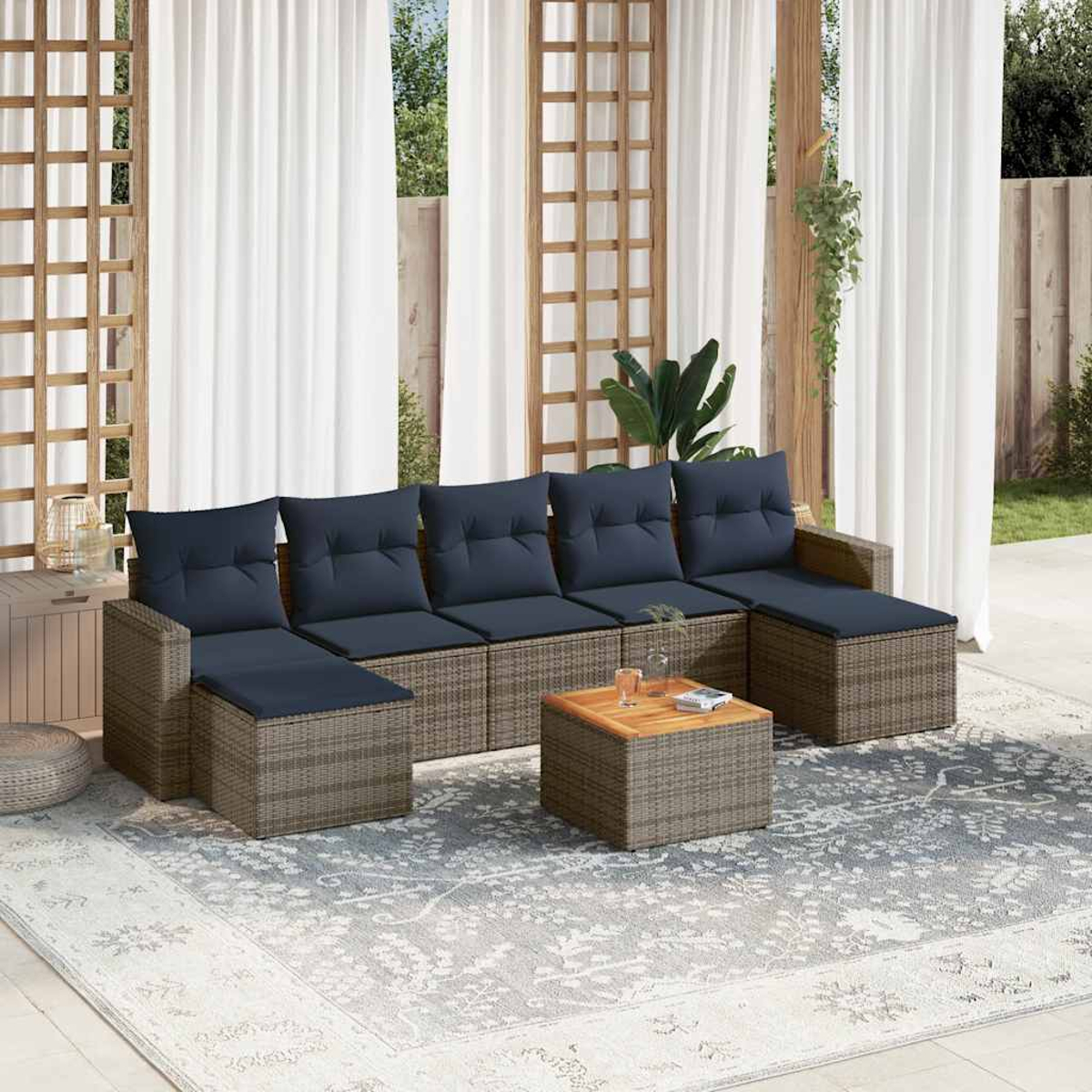 Conjunto de asientos al aire libre con cojines azules, mesa de centro y alfombra estampada. Cortinas blancas y celosía de madera.