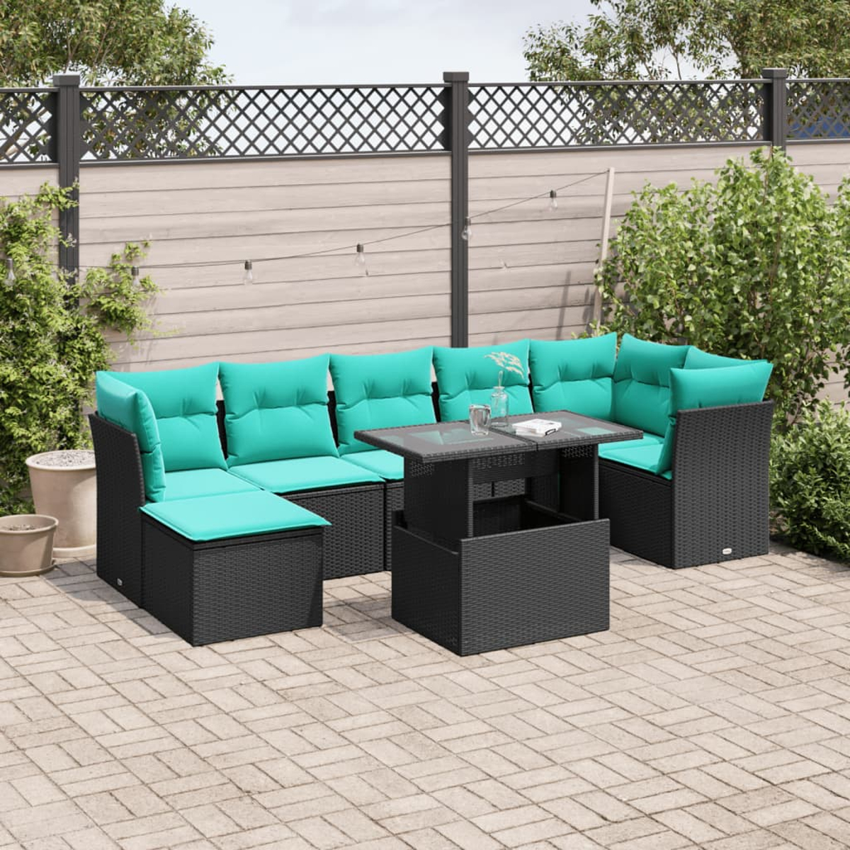 Garten-Terrassenset mit schwarzen Korbmöbeln, türkisfarbenen Kissen und einem Tisch mit Glasplatte. Vor einem Zaun und Grün.