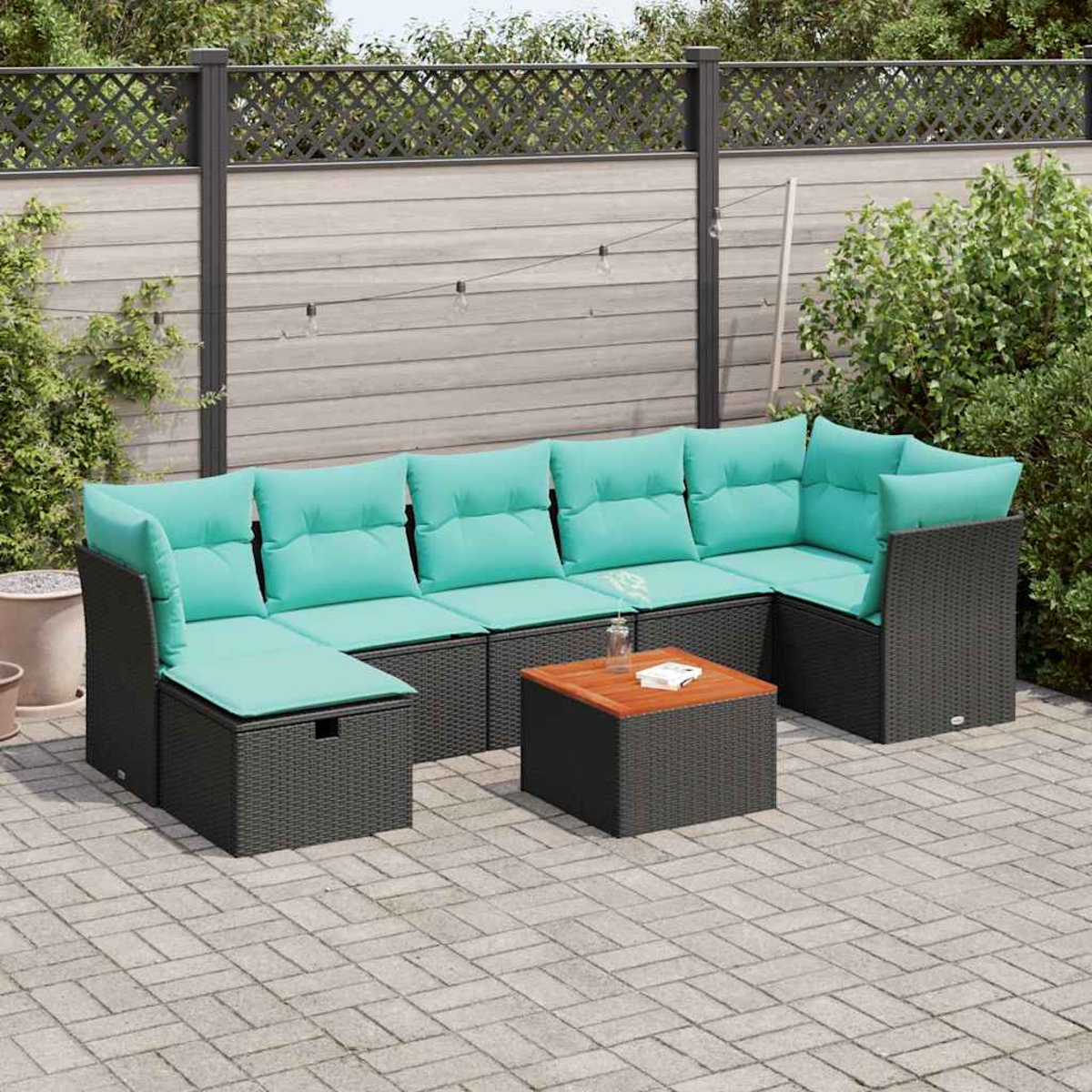 Outdoor-Ecksofa mit türkisfarbenen Kissen und einem Holztisch auf einer Ziegelpflasterung. Im Hintergrund ein Zaun und Pflanzen.